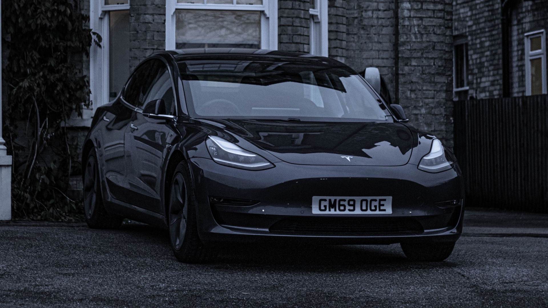 Black Tesla Model 3 parked outside a brick building HD Wallpaper