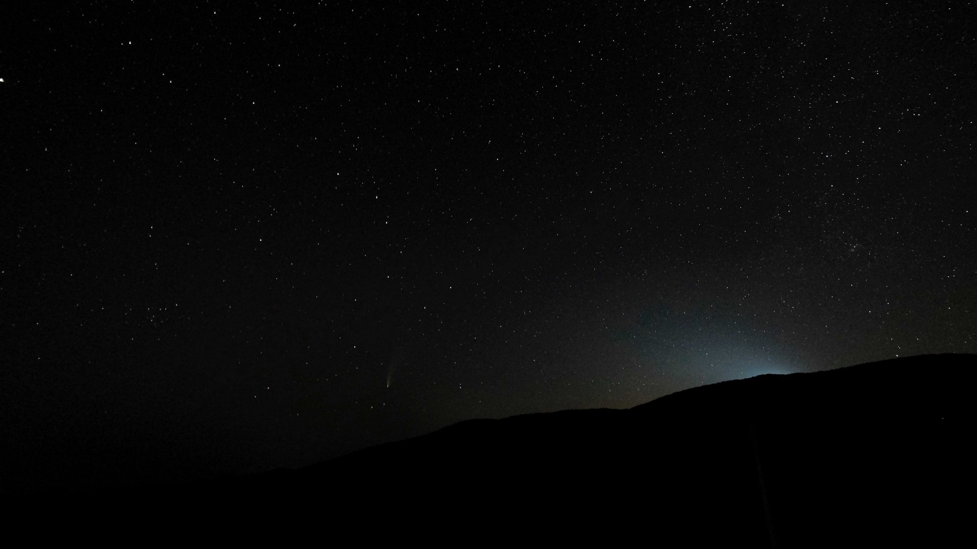 Starry night sky over a silhouetted mountain range HD Wallpaper