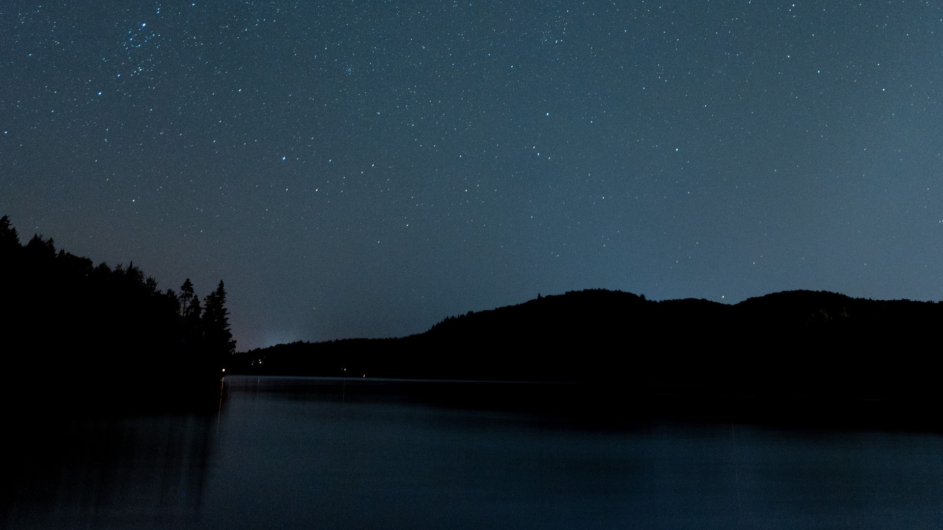 Night sky over a lake with silhouetted trees and hills HD Wallpaper