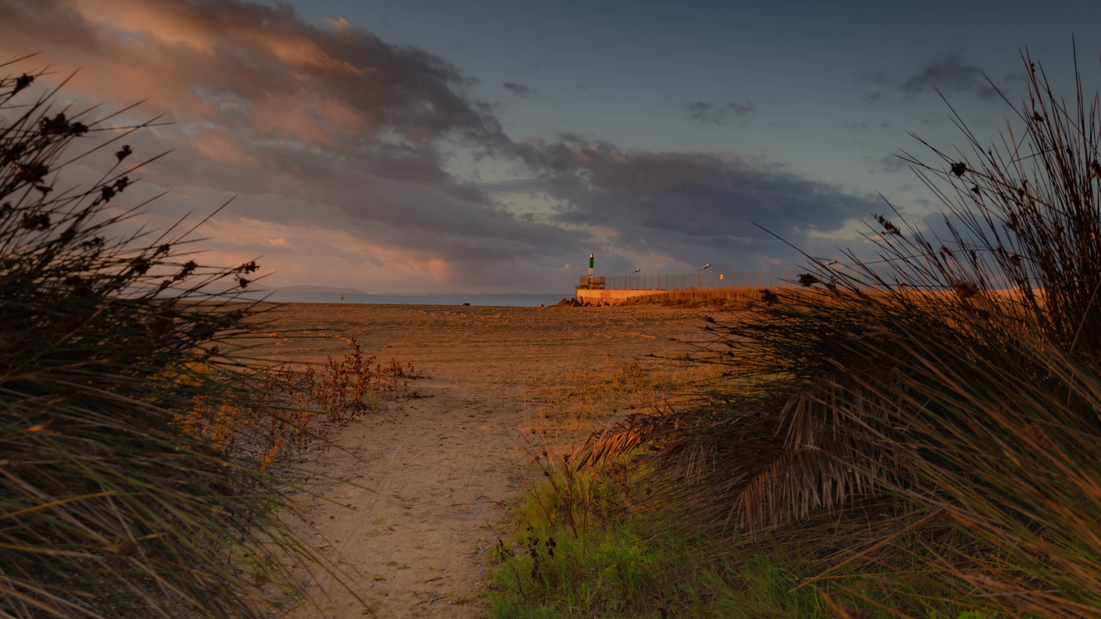 Beach path at sunset with lighthouse HD Wallpaper