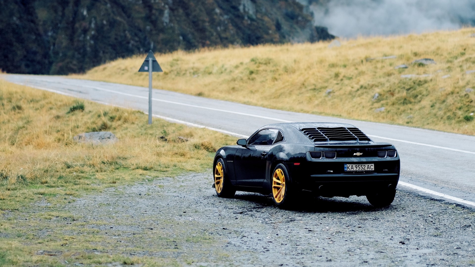 Black Chevrolet Camaro with gold rims on a mountain road HD Wallpaper