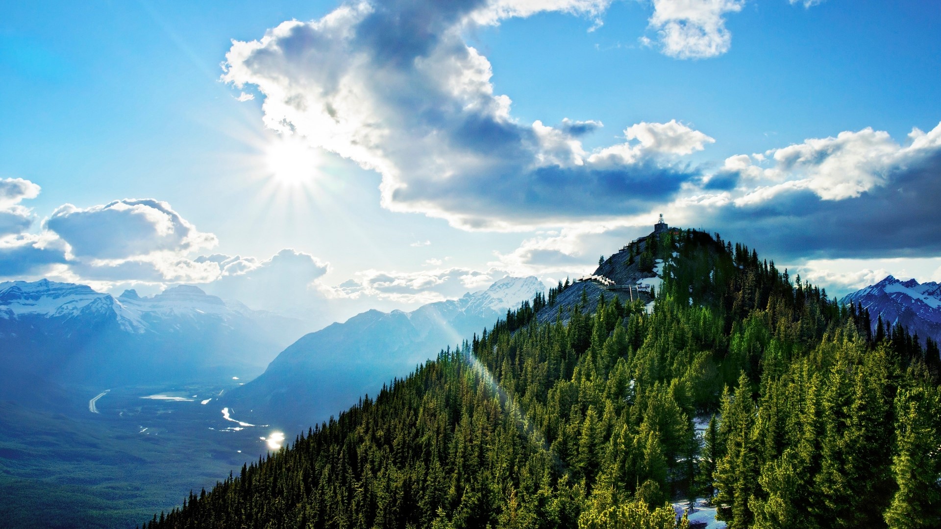 Mountain peak with trees and sunlit clouds HD Wallpaper