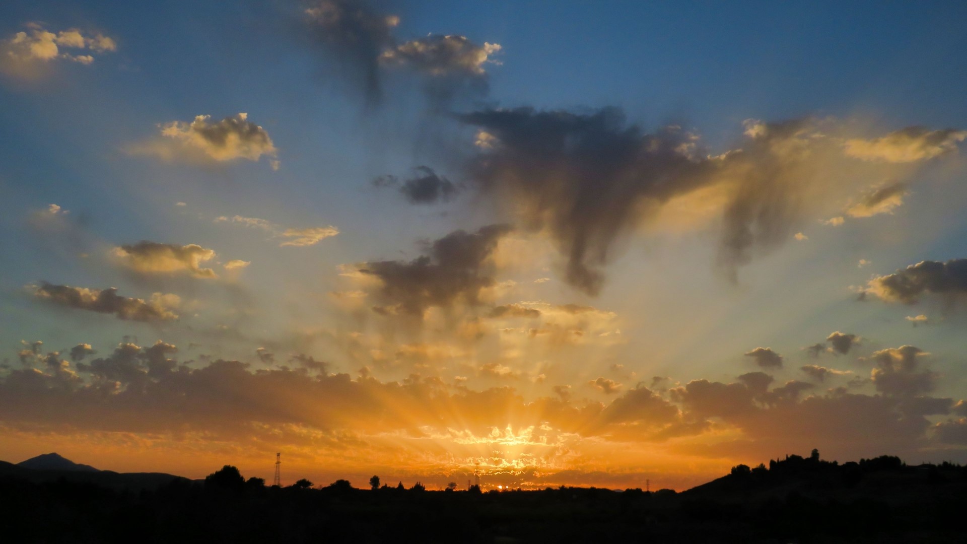Sunset with sun rays over a silhouetted landscape HD Wallpaper