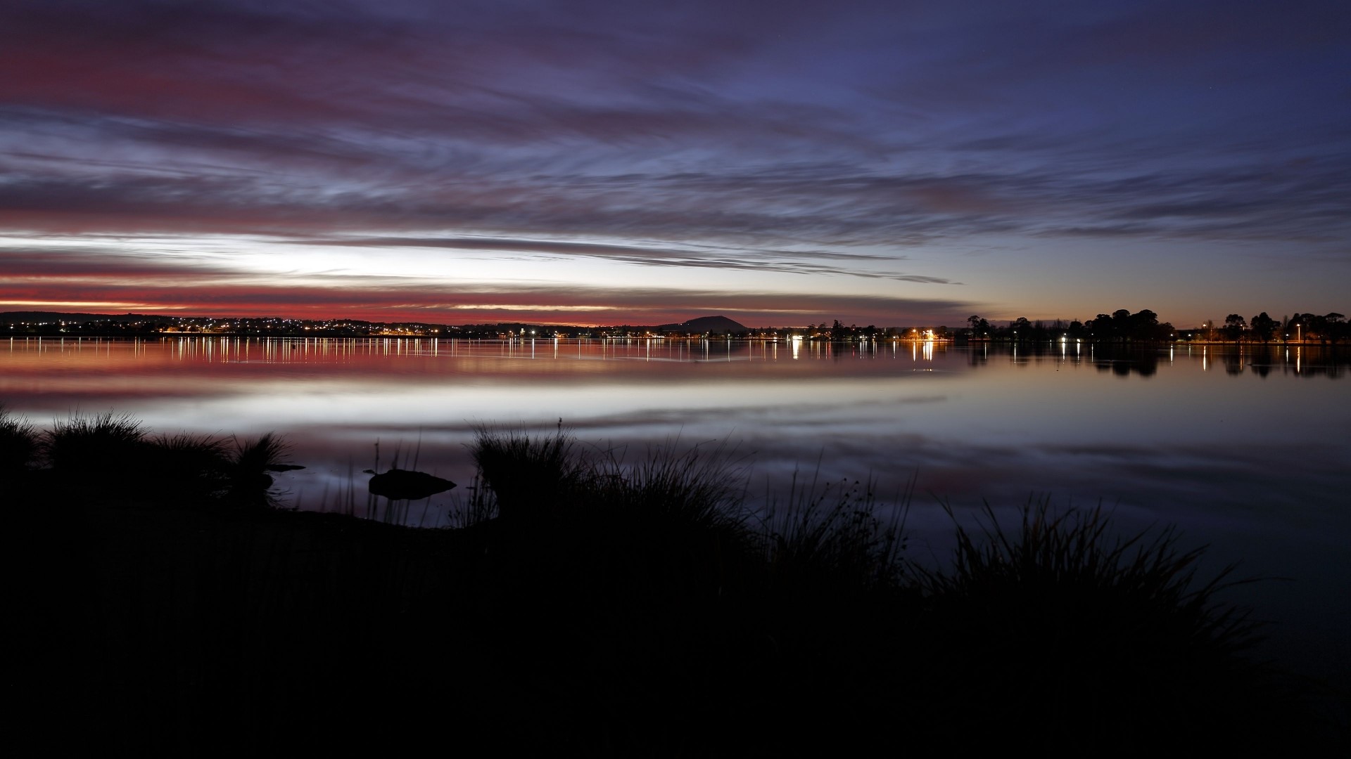 Sunset over a lake with city lights HD Wallpaper