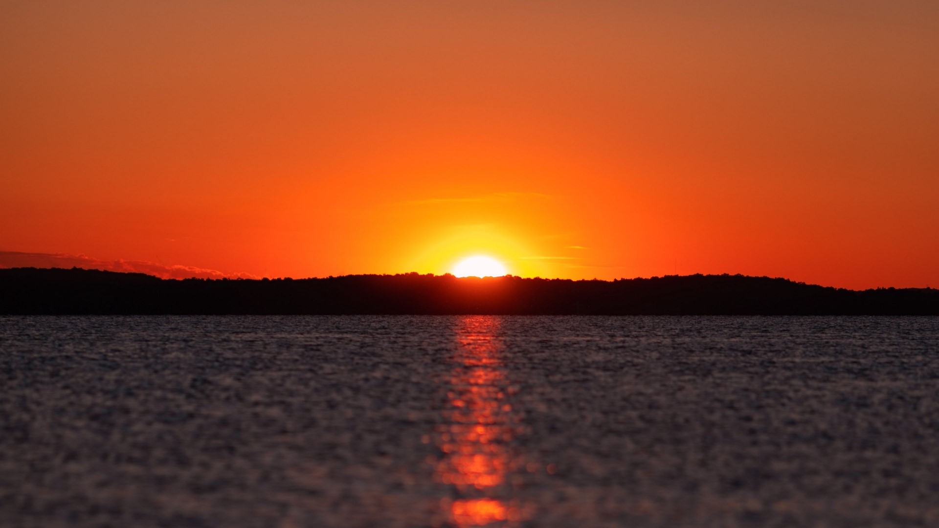 Sunset over a body of water with a silhouetted horizon HD Wallpaper