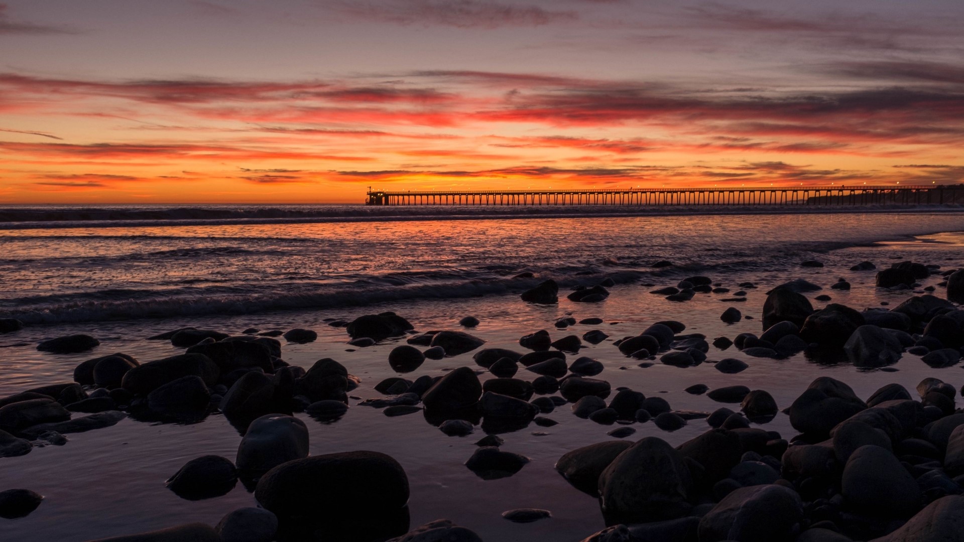 Sunset over the ocean with a pier and rocks HD Wallpaper