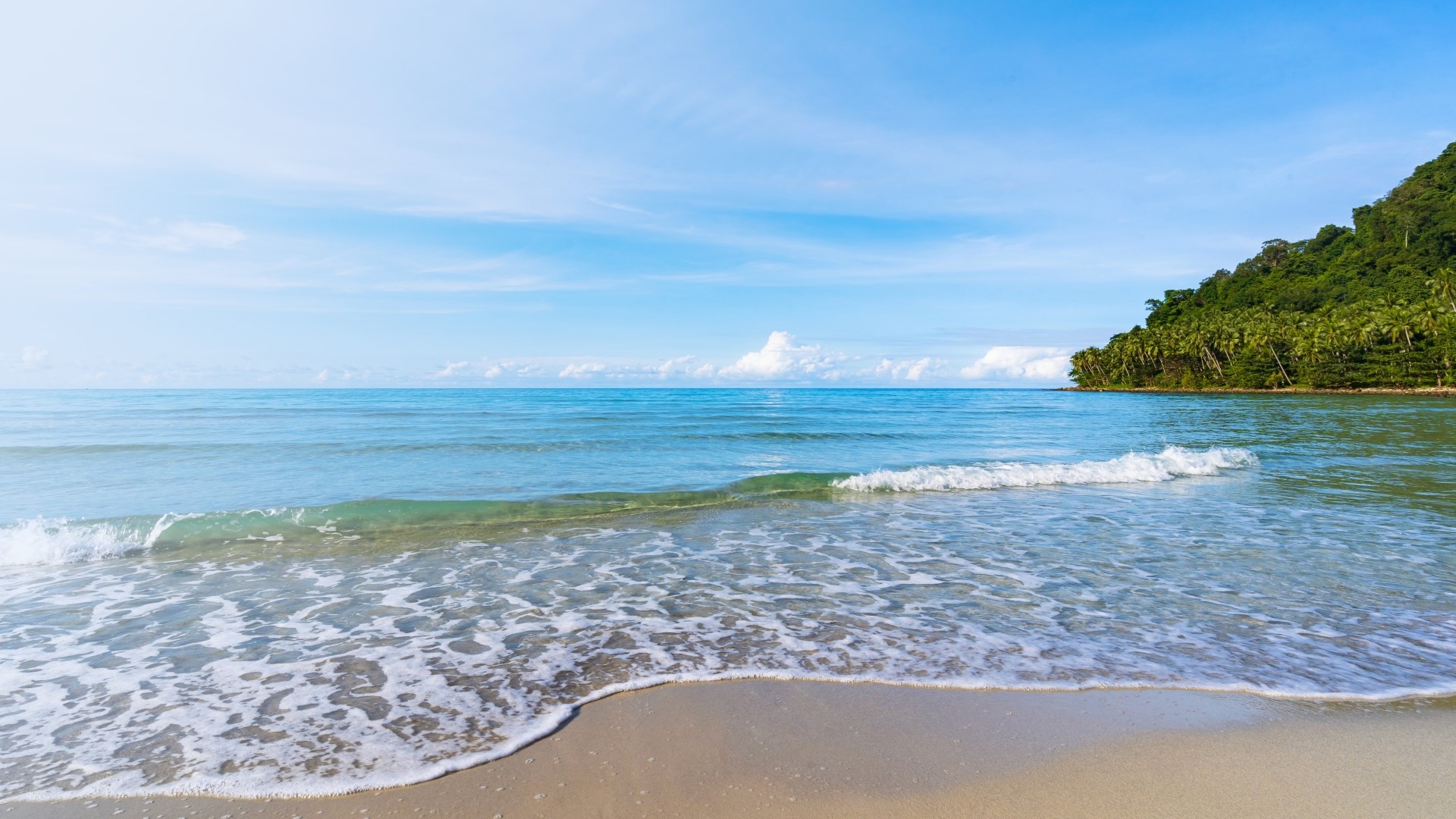 Ocean waves on a sandy beach with a tropical island in the background HD Wallpaper