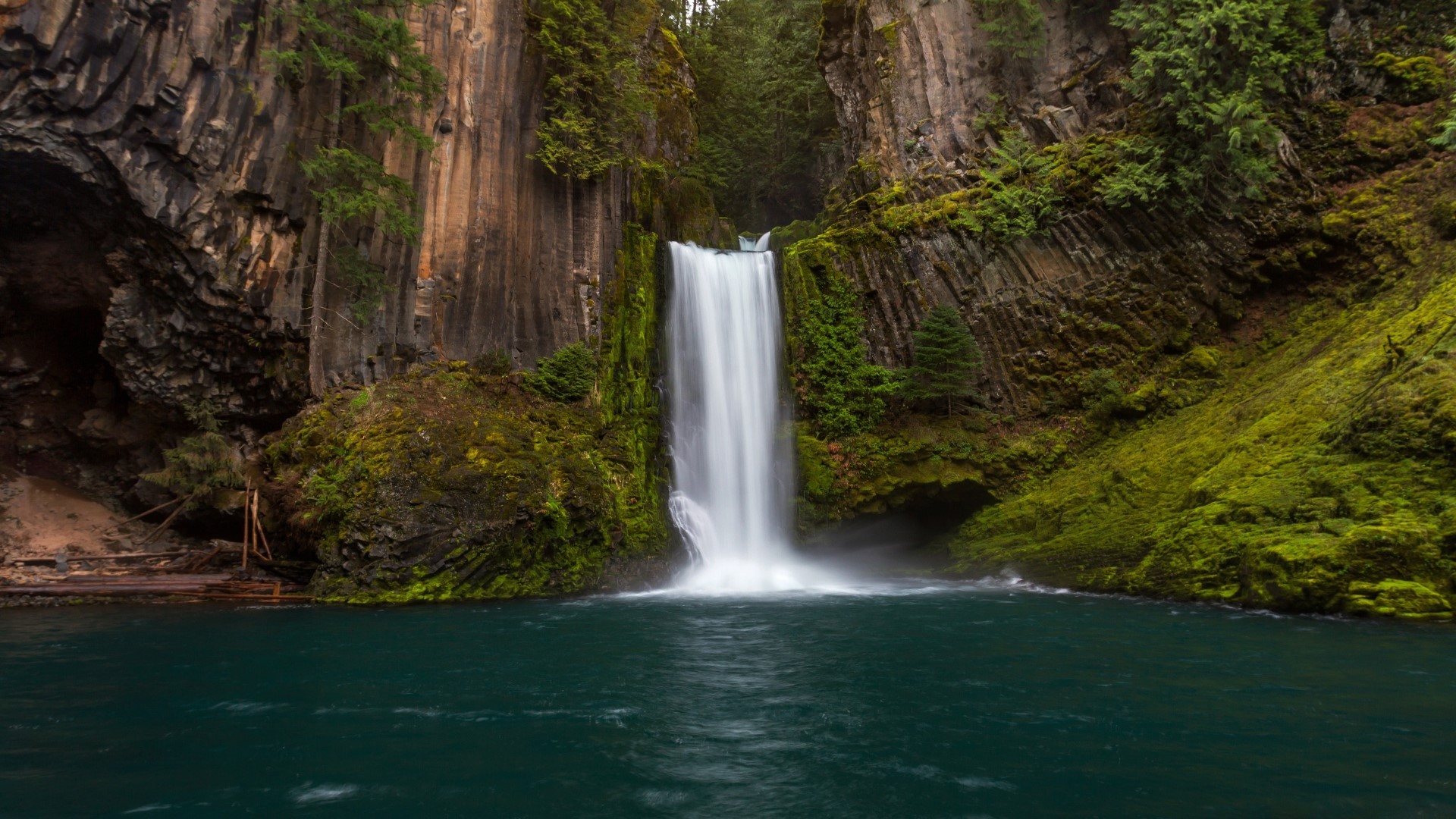 Waterfall cascading into a turquoise pool surrounded by mossy cliffs HD Wallpaper