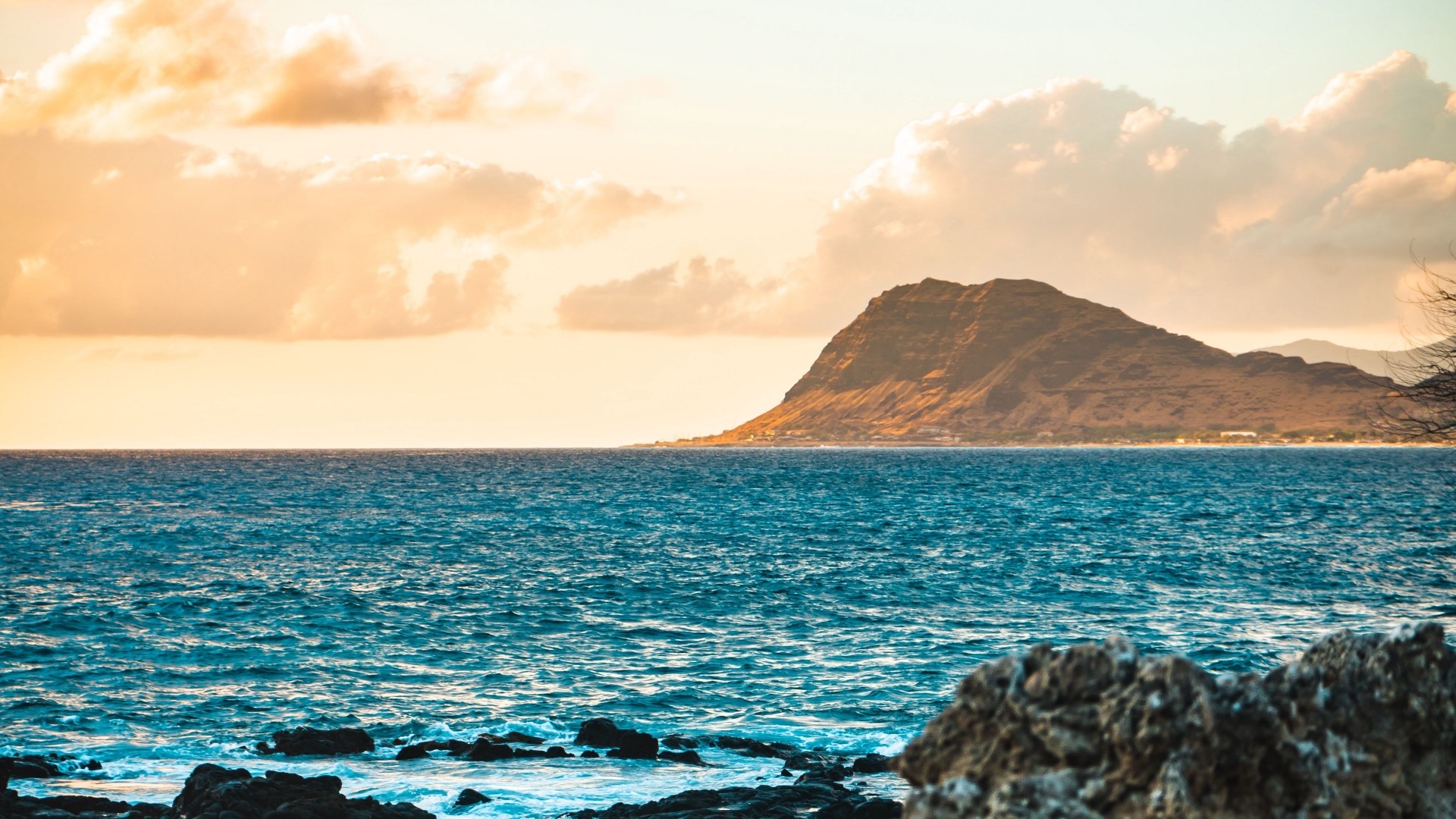 Ocean waves crashing on rocks with a mountain in the distance HD Wallpaper