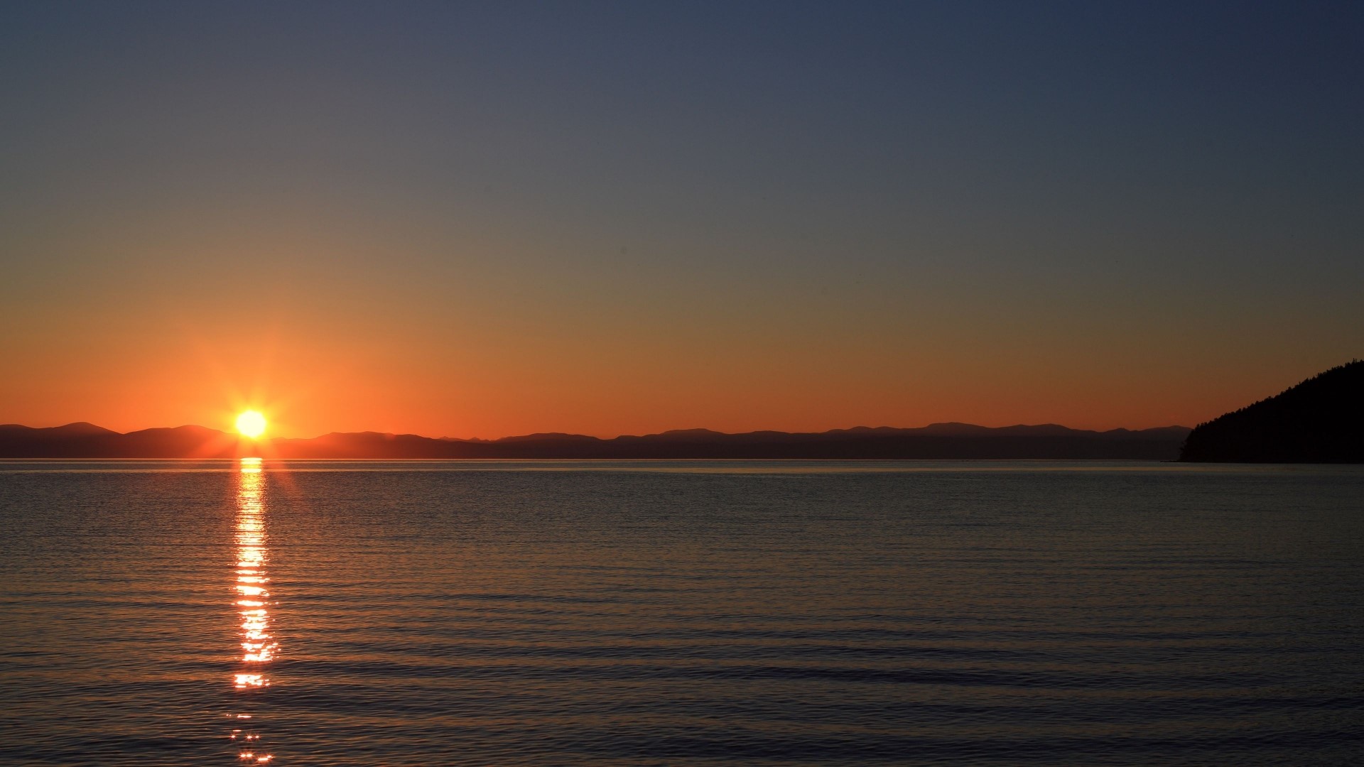 Sunset over a calm lake with distant mountains HD Wallpaper