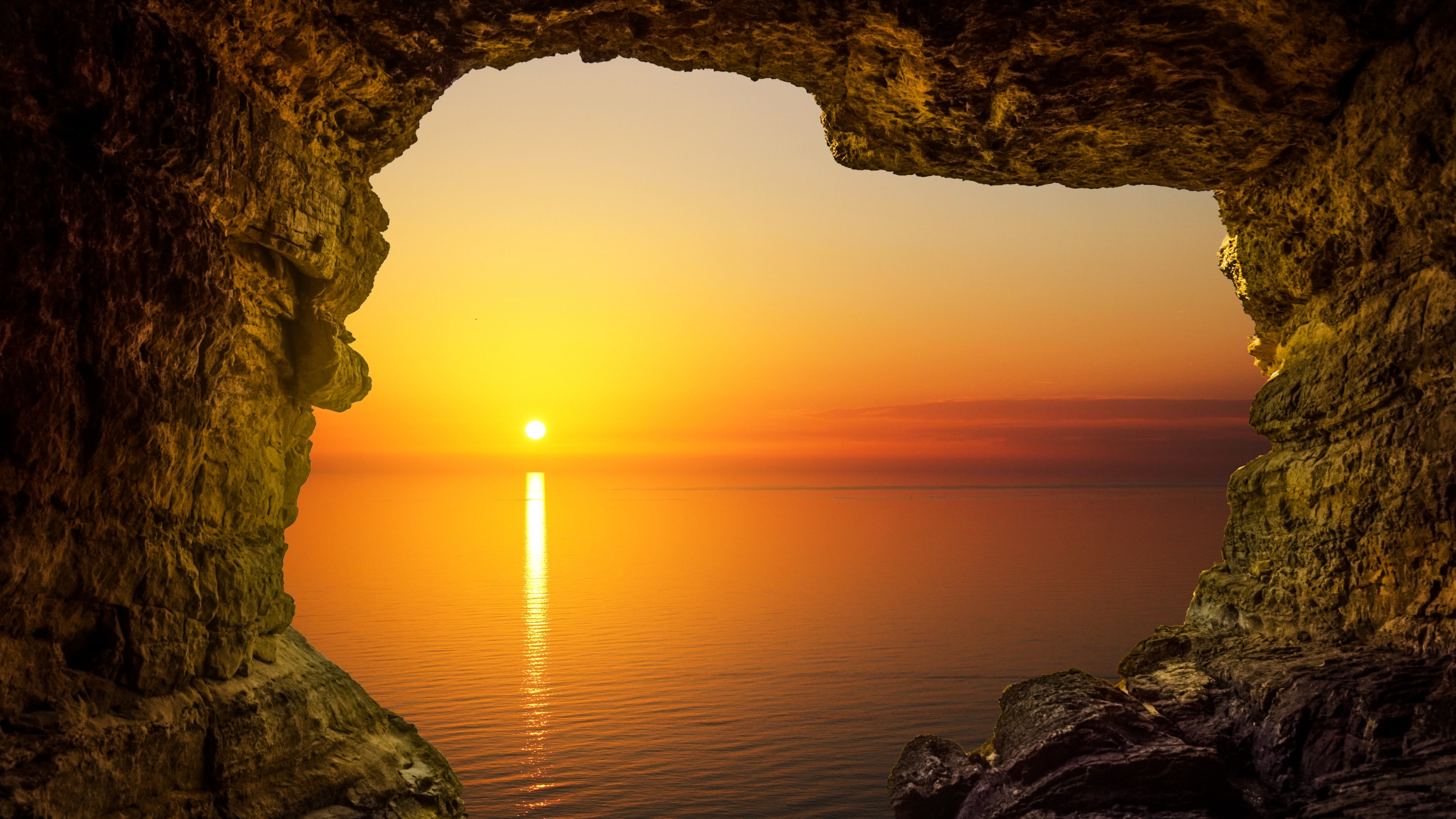 Cave entrance overlooking a 4K sunset over the ocean HD Wallpaper