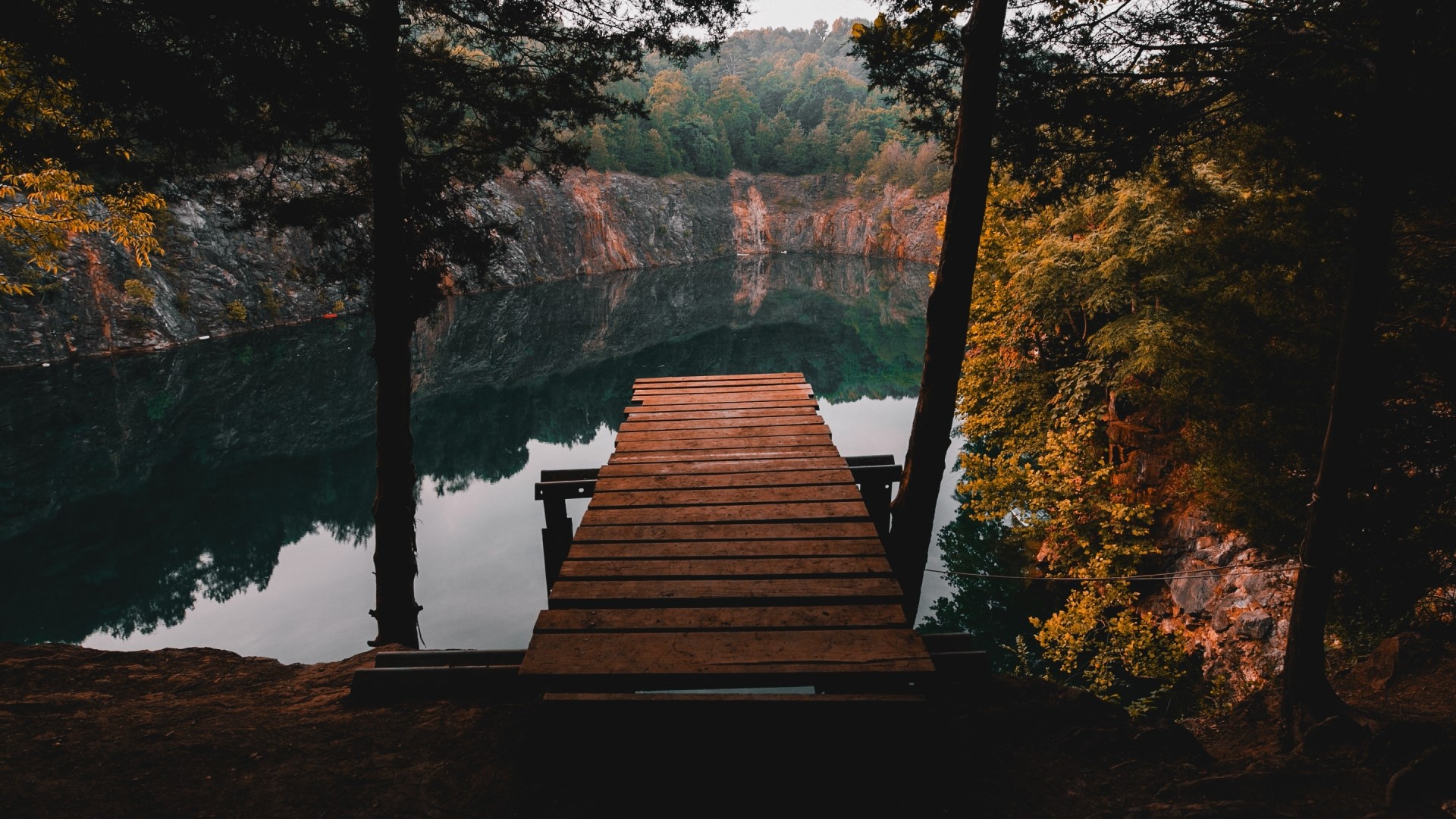 Wooden dock on a quarry lake surrounded by trees HD Wallpaper