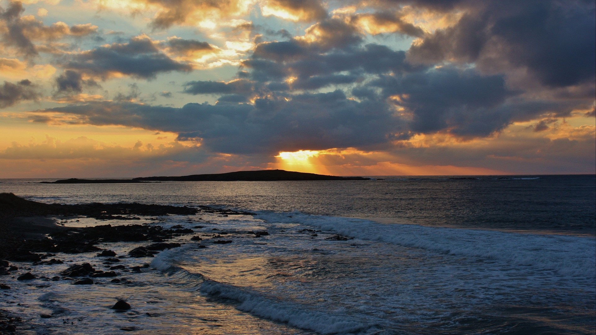 Sunset over the ocean with waves and island HD Wallpaper