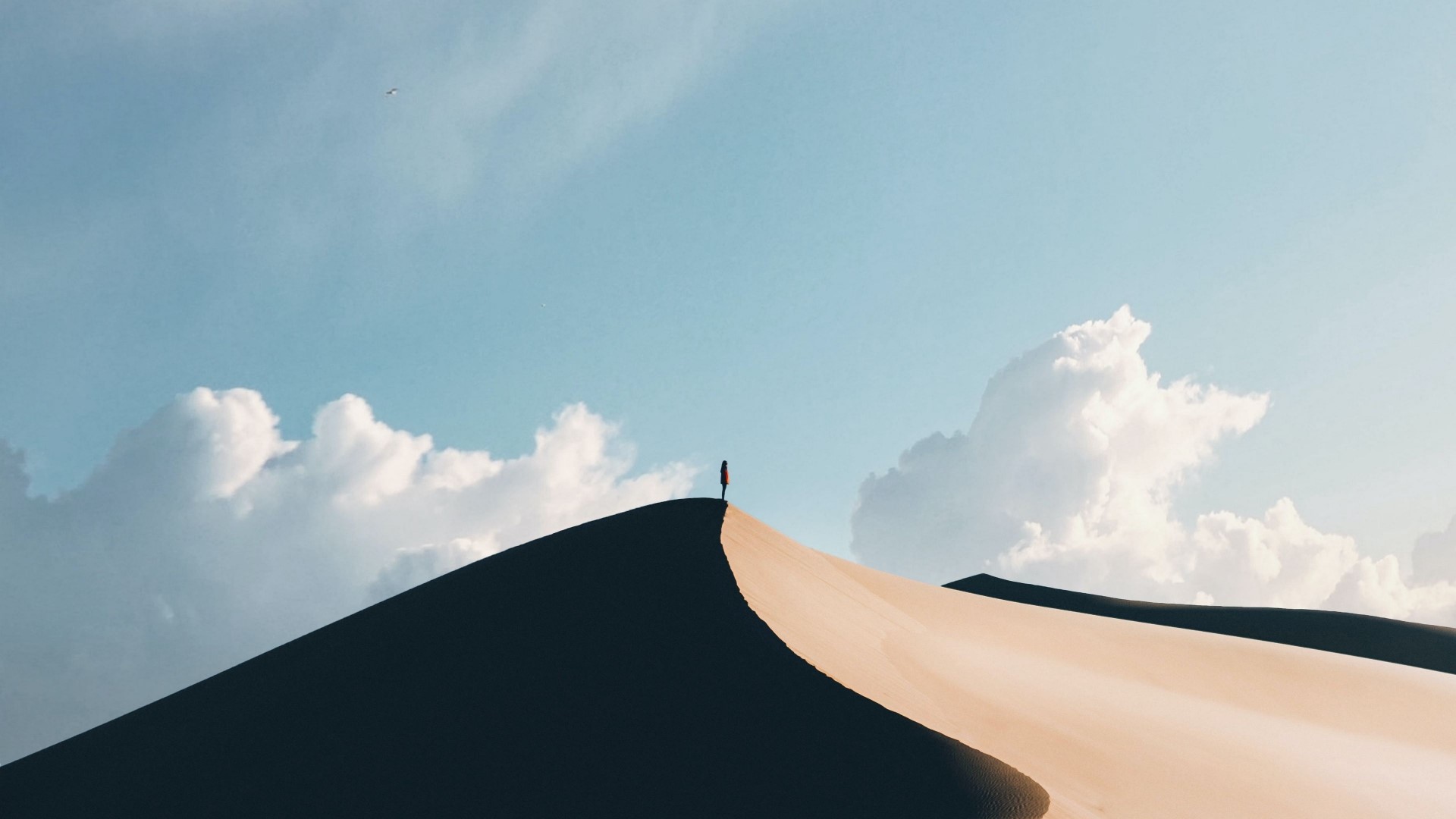 Person standing on a desert dune under a cloudy sky HD Wallpaper