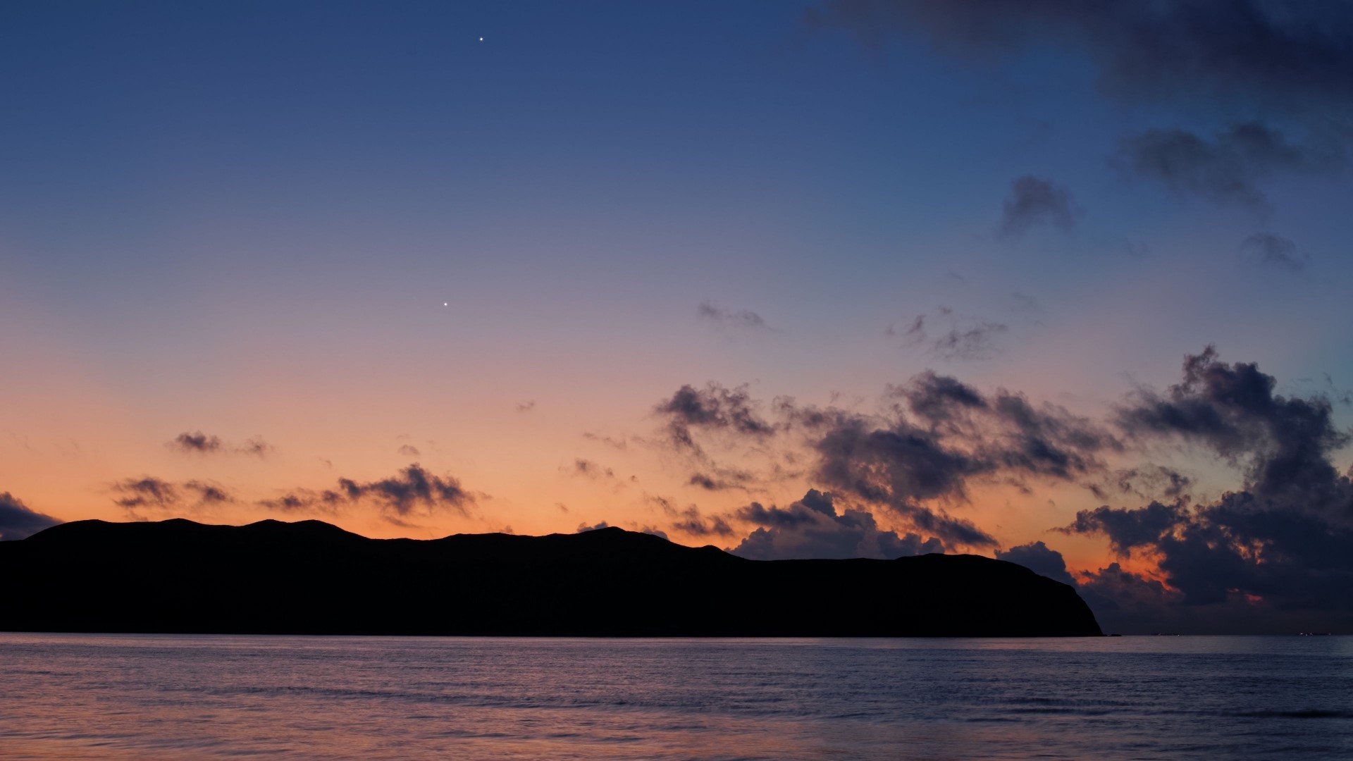 Sunset over the ocean with a silhouetted island HD Wallpaper