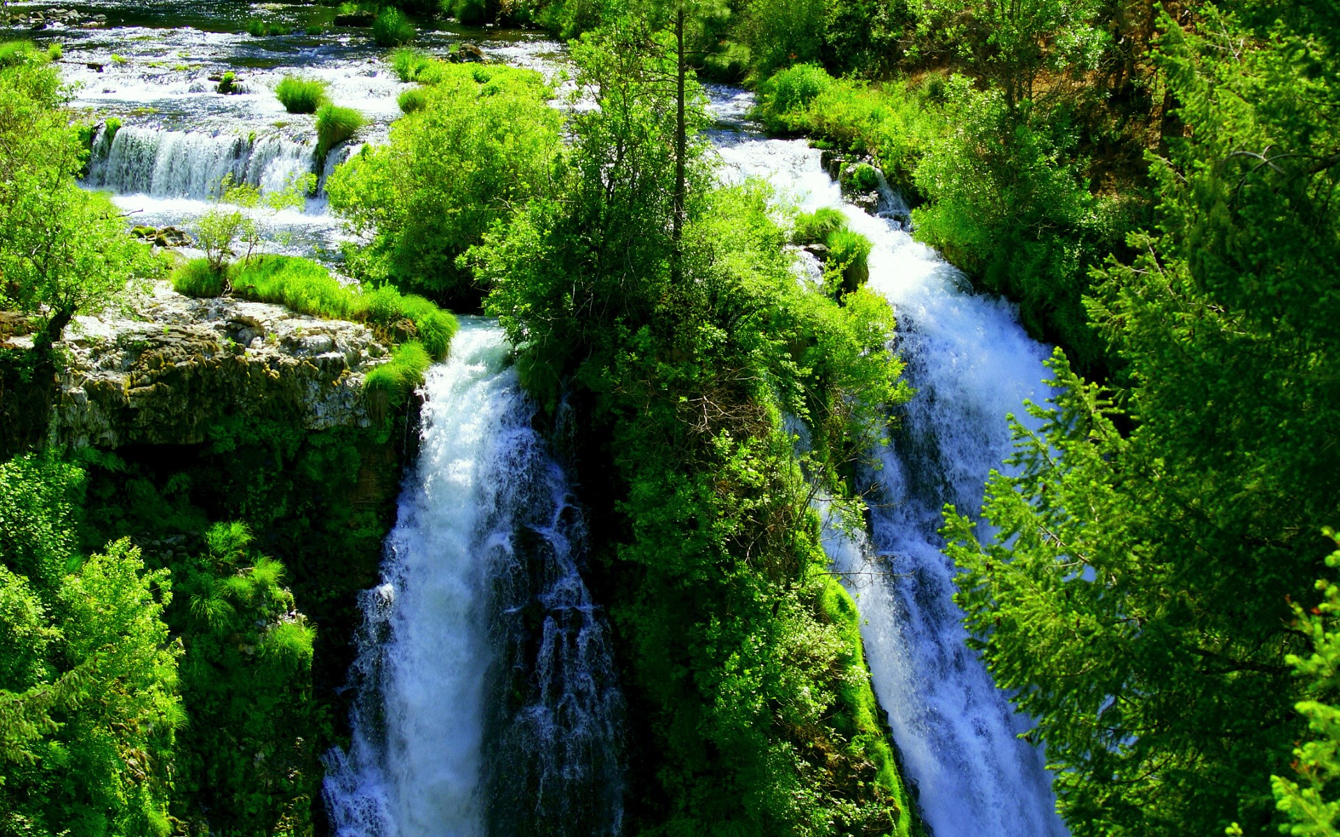 Waterfalls cascade through a lush green forest. HD Wallpaper