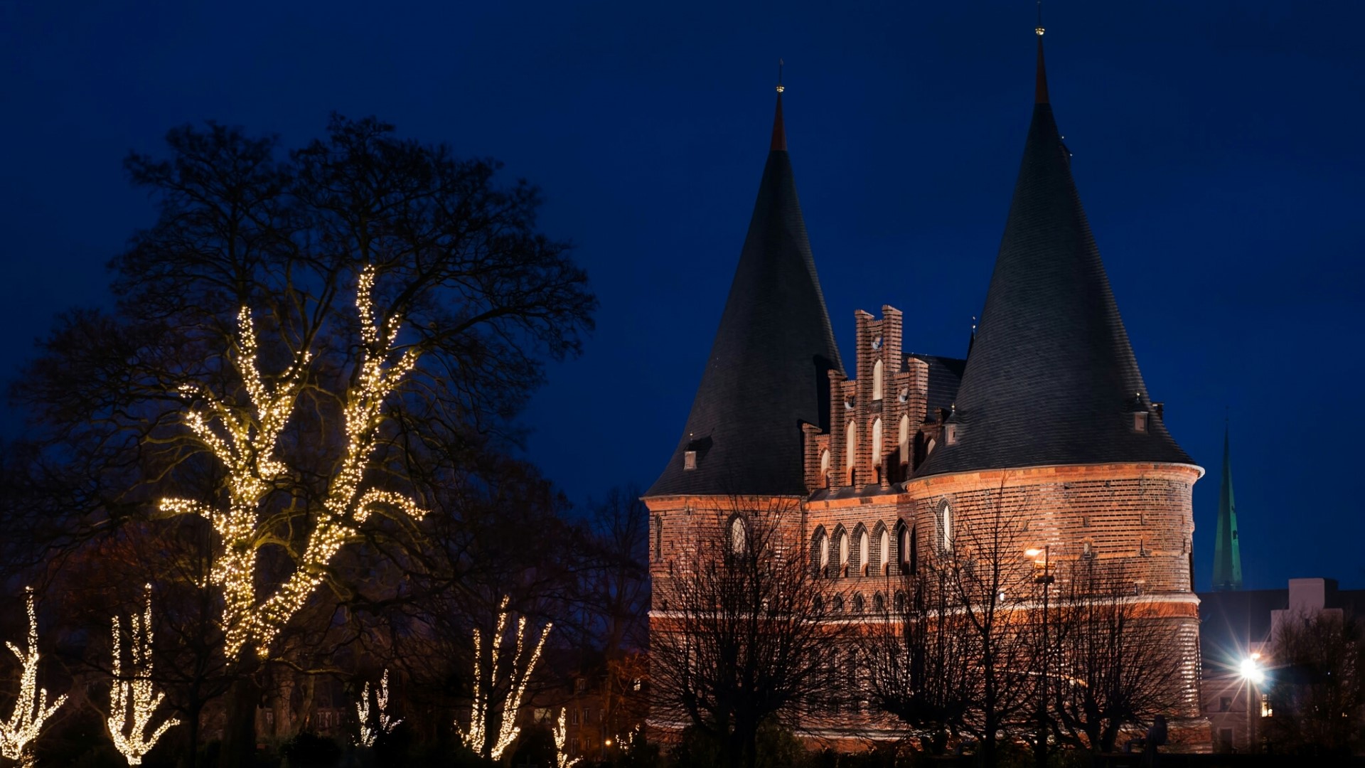 Brick gate towers with conical roofs decorated with lights at night HD Wallpaper