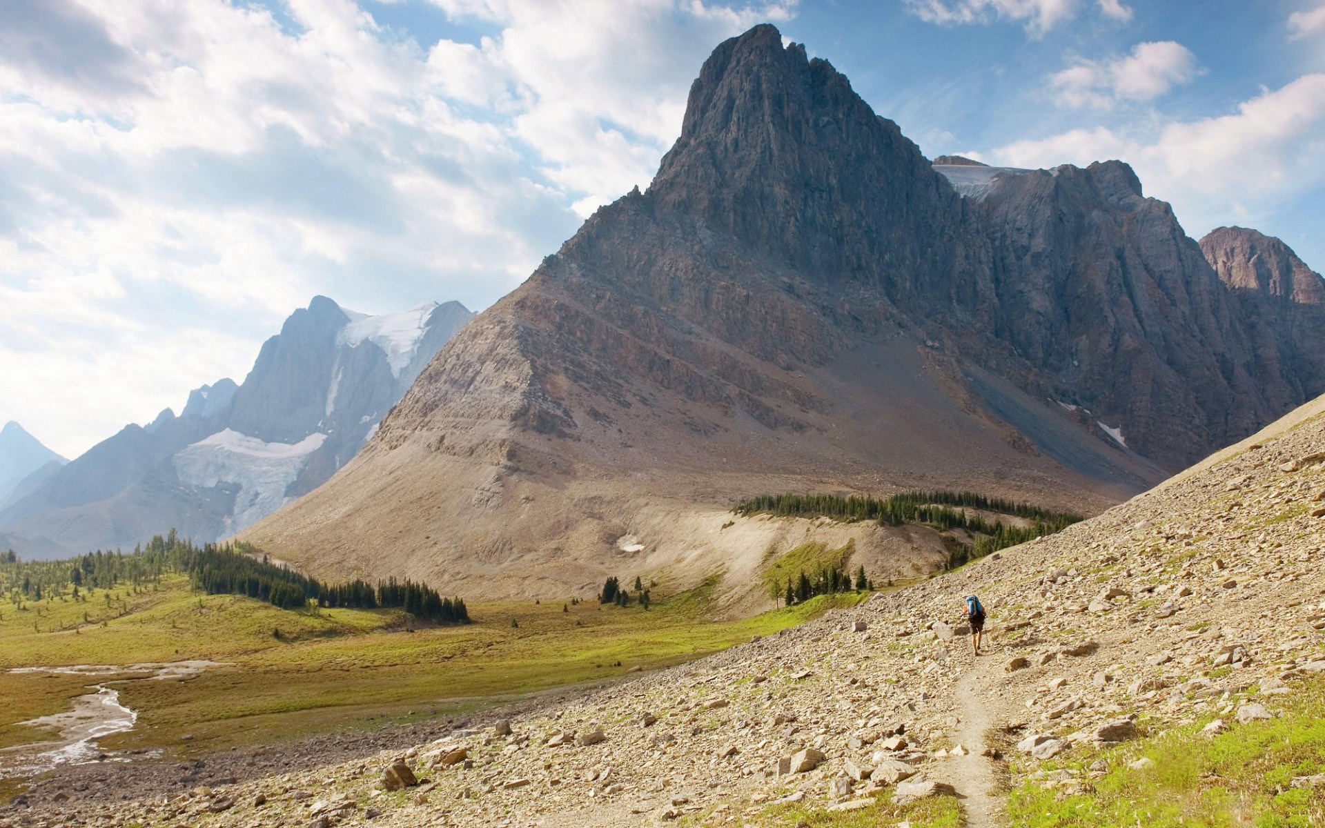 Hiker on a rocky mountain trail with glaciers in the background HD Wallpaper