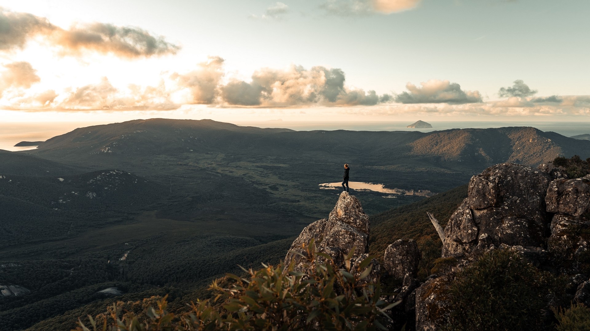 Person standing on a rocky peak overlooking a valley HD Wallpaper