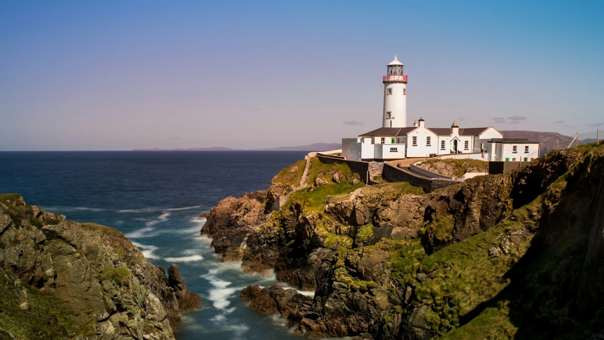 White lighthouse on a rocky cliff overlooking the ocean HD Wallpaper
