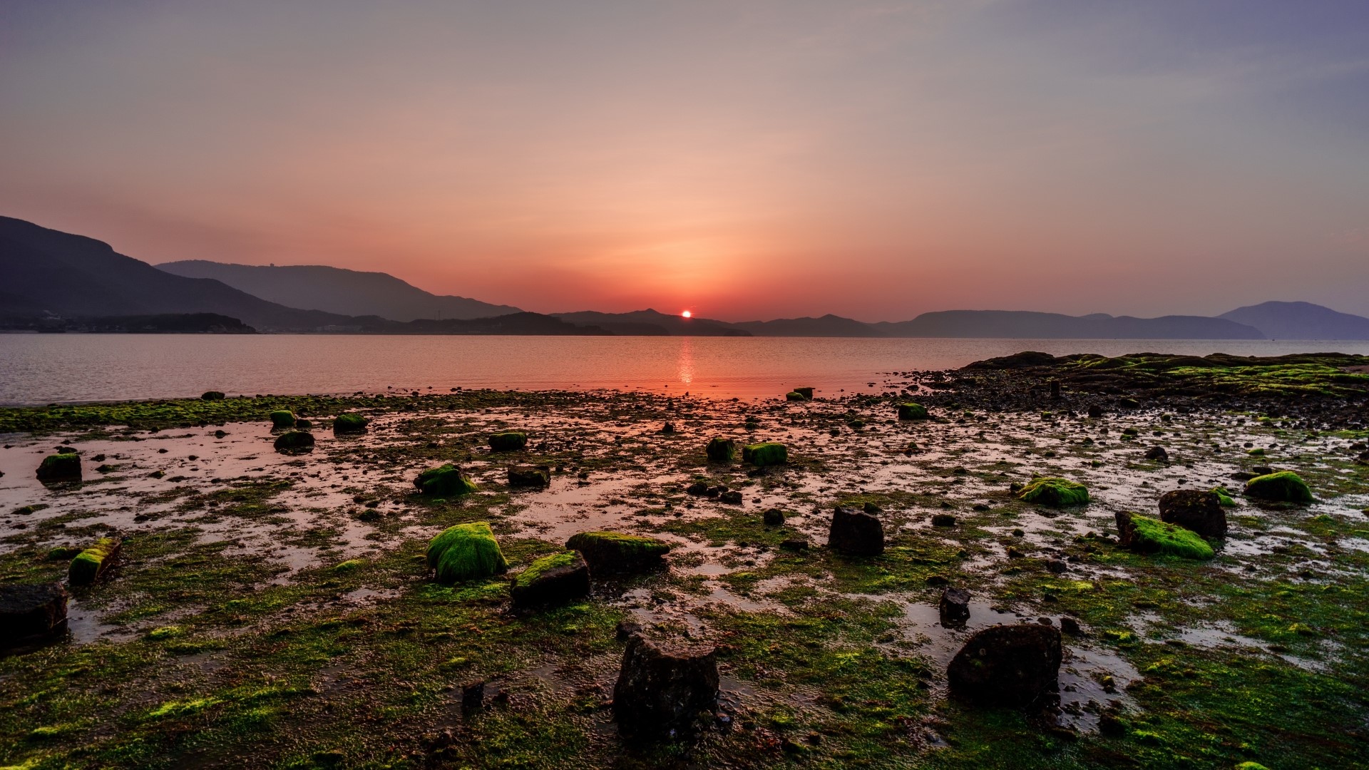 Sunset over the ocean with mountains and rocky shore HD Wallpaper