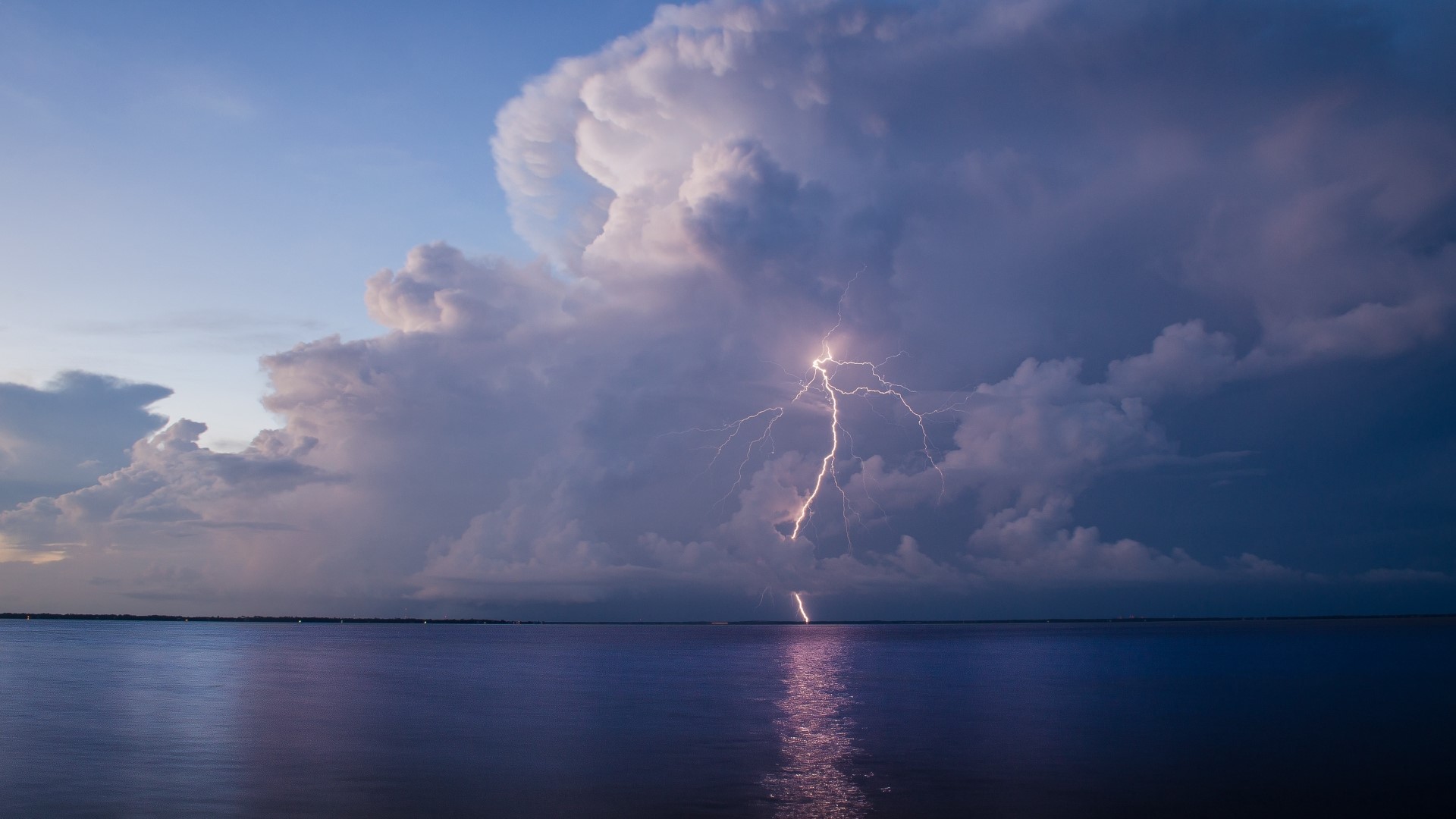 Lightning strikes over a calm body of water during a storm HD Wallpaper