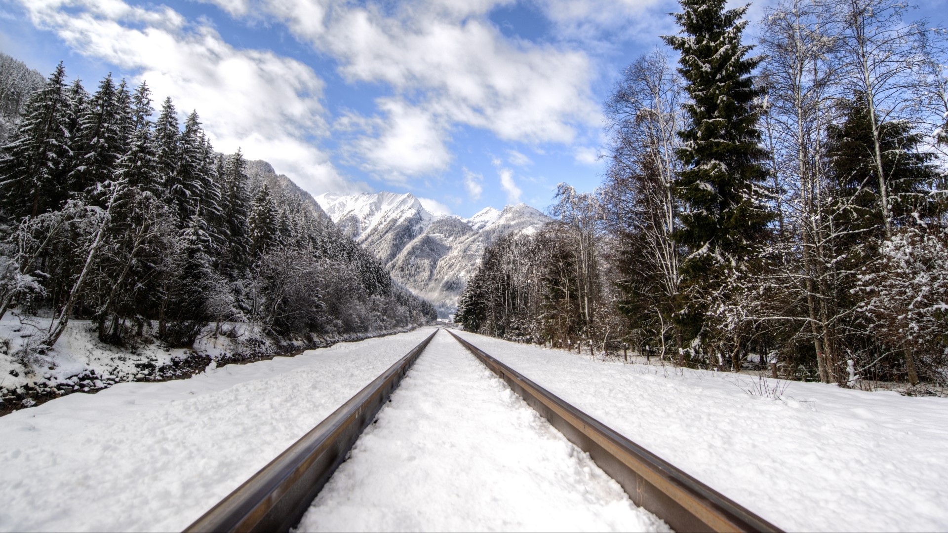 Snowy railway tracks leading to snow-covered mountains HD Wallpaper