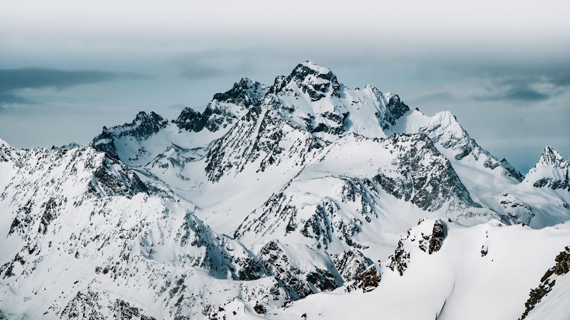 Snow-covered mountain range under a cloudy sky HD Wallpaper