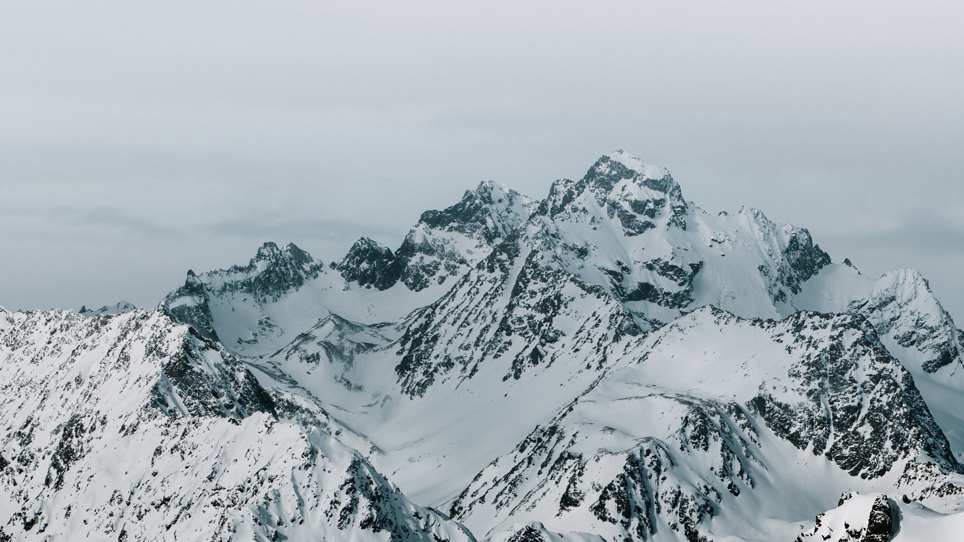 Snow-covered mountain peaks under a cloudy sky HD Wallpaper