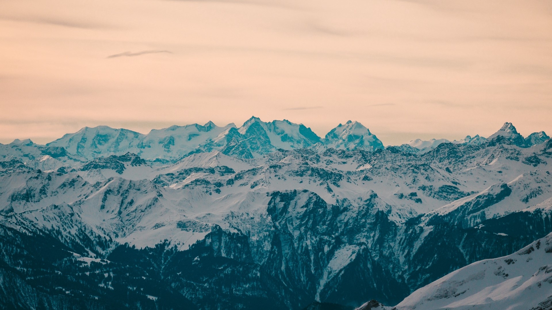 Snow-covered mountain range under a pale sky HD Wallpaper