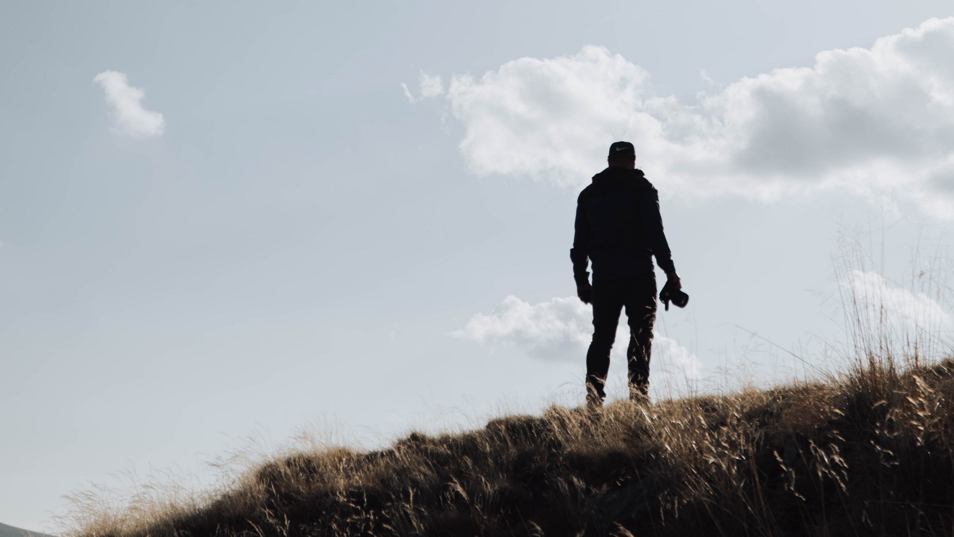 Silhouette of a person holding a camera on a grassy hill HD Wallpaper