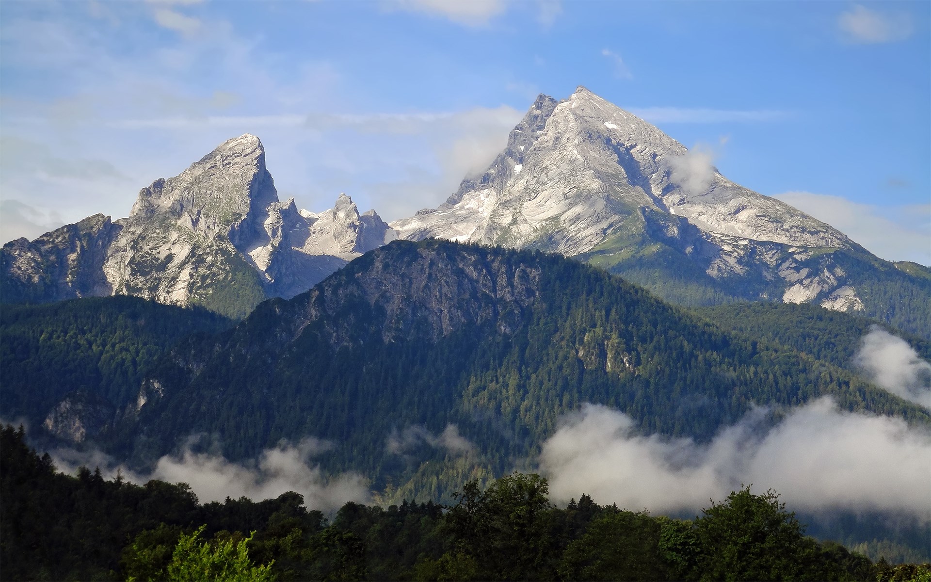 Jagged mountain peaks with green forested slopes and clouds HD Wallpaper