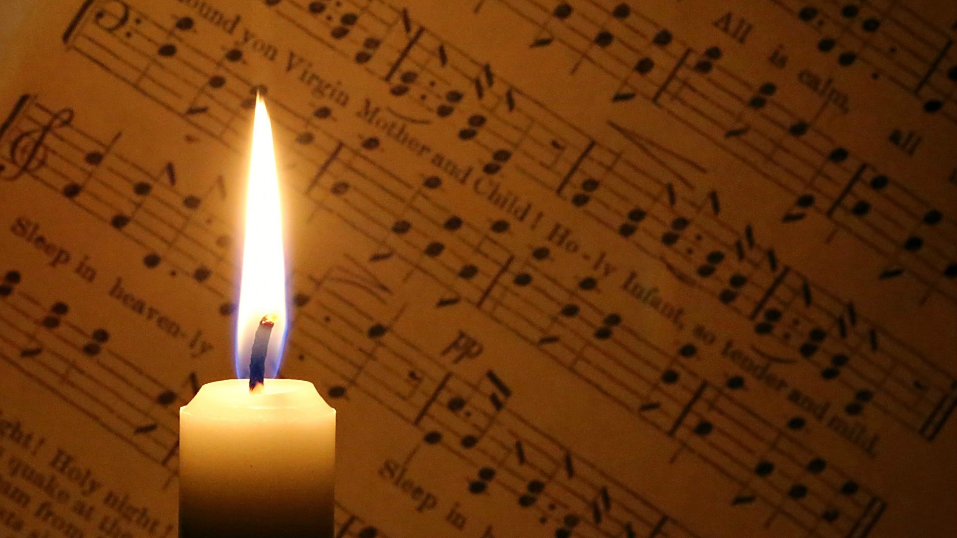 Candle burning in front of sheet music HD Wallpaper
