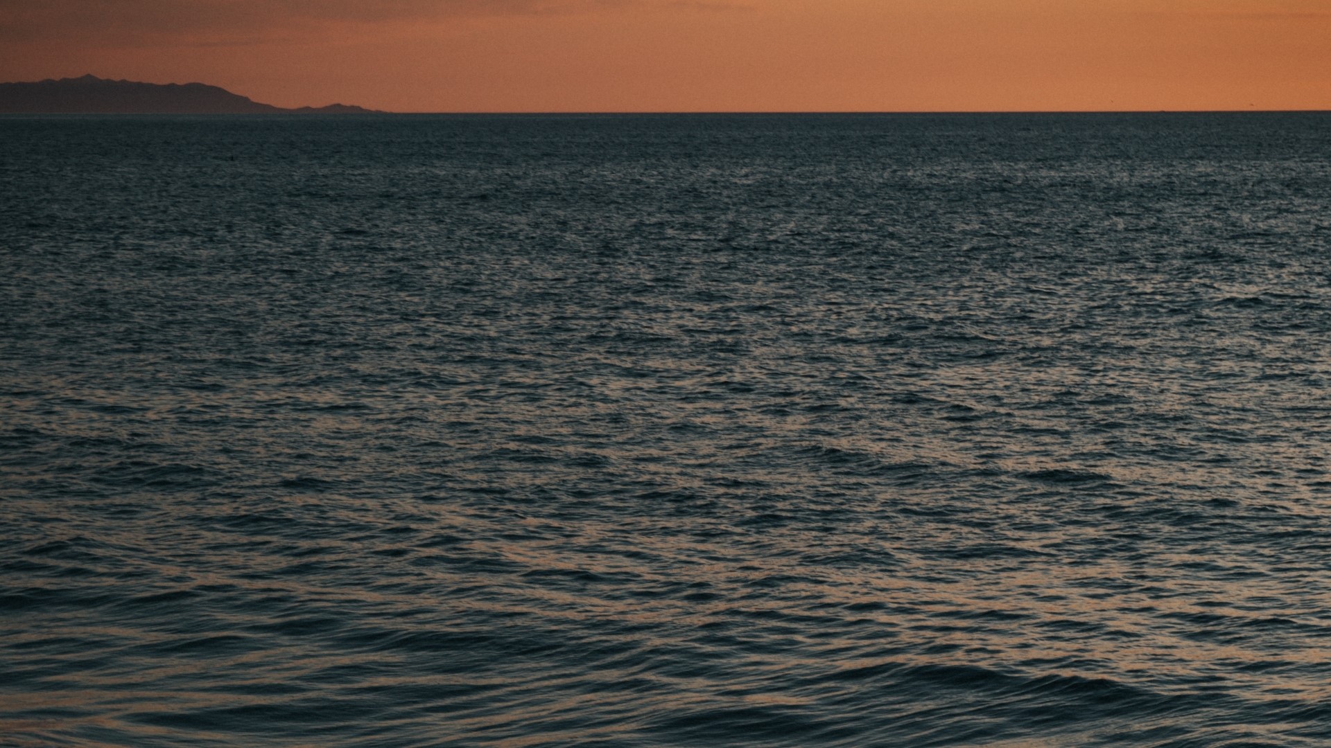 Ocean waves at sunset with distant mountains HD Wallpaper