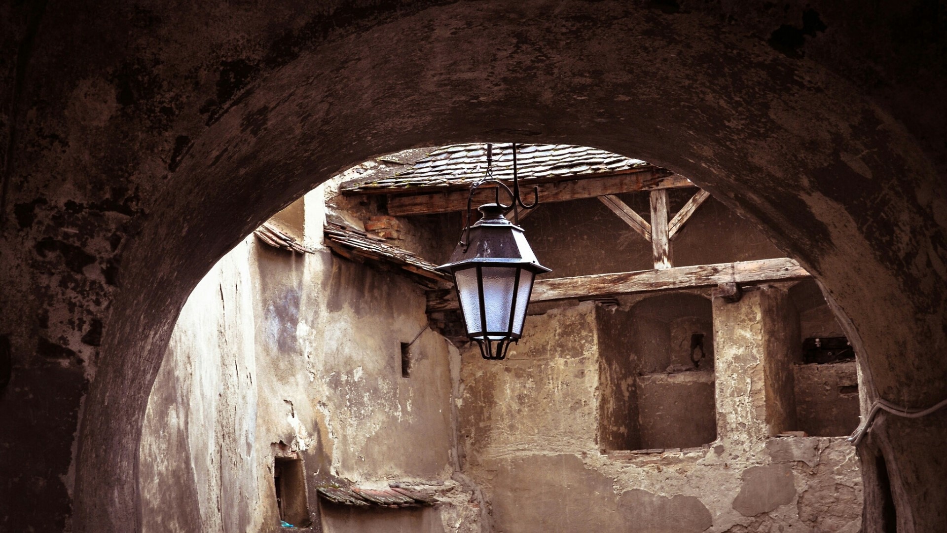 Old stone archway with hanging lantern and tiled roof HD Wallpaper