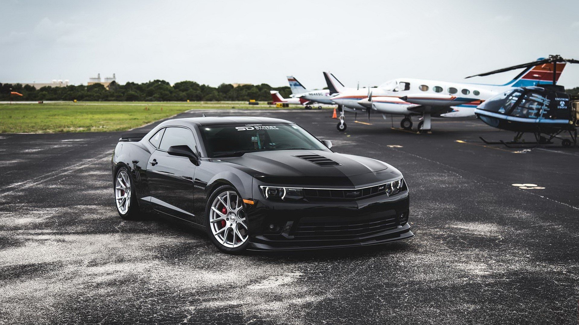 Black Chevrolet Camaro parked at an airfield with planes HD Wallpaper