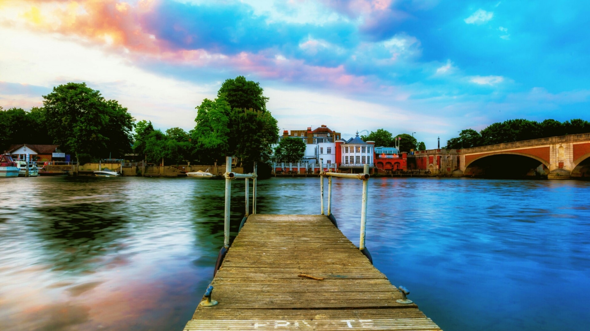 Wooden pier on a river with a bridge in the background HD Wallpaper