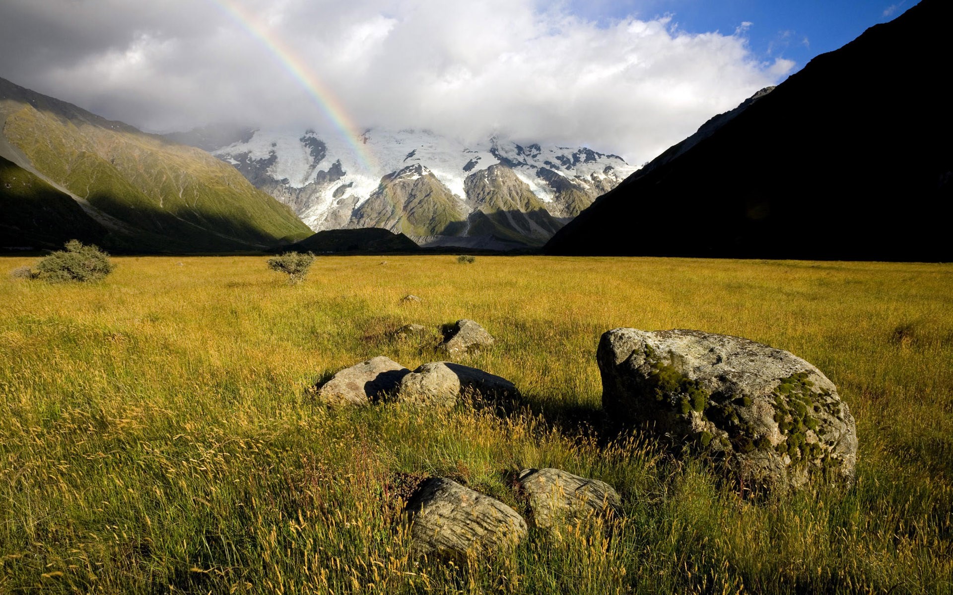 Rainbow over snowy mountains and a grassy field HD Wallpaper