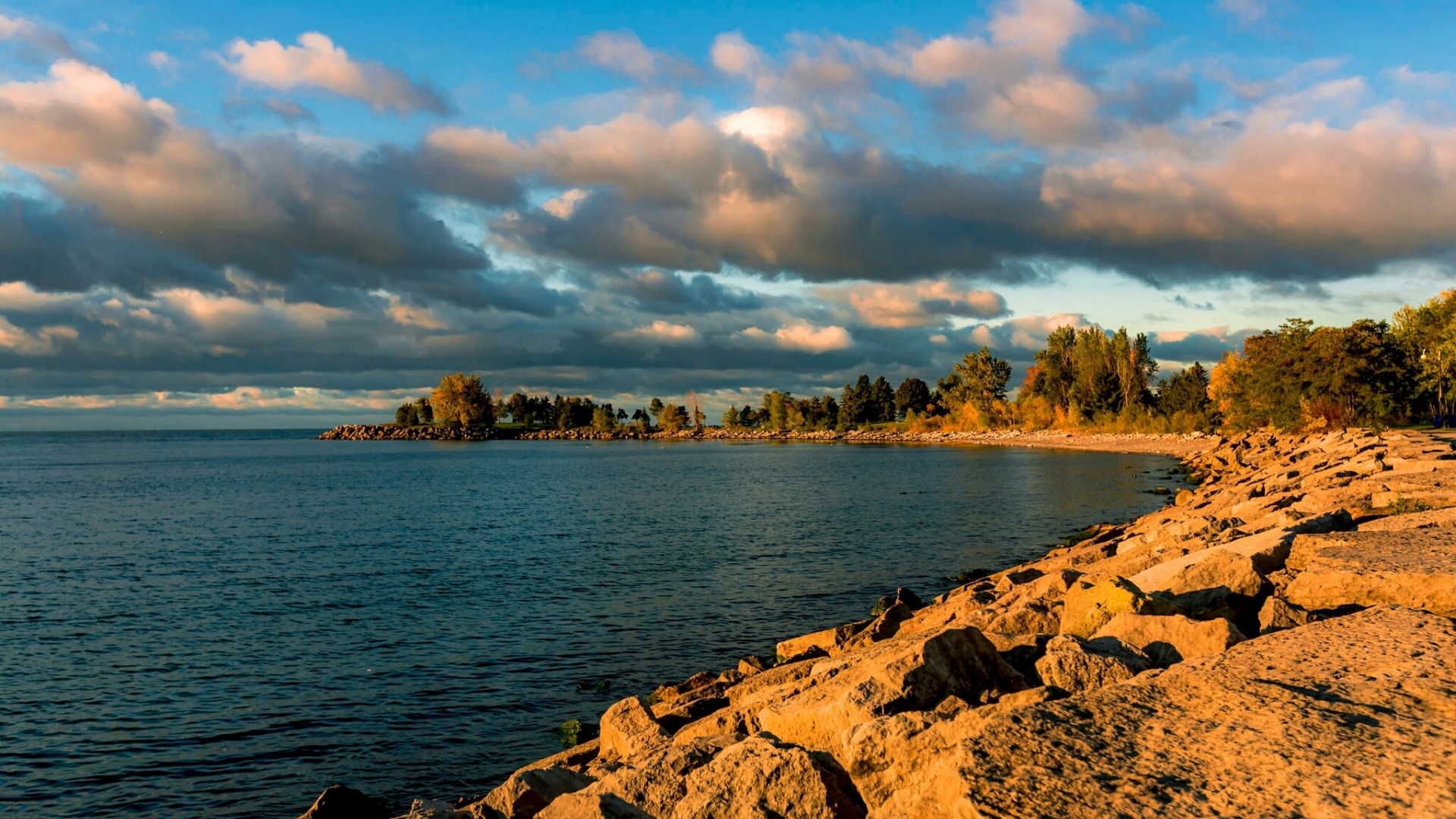 Rocky shoreline with calm sea and cloudy sky HD Wallpaper