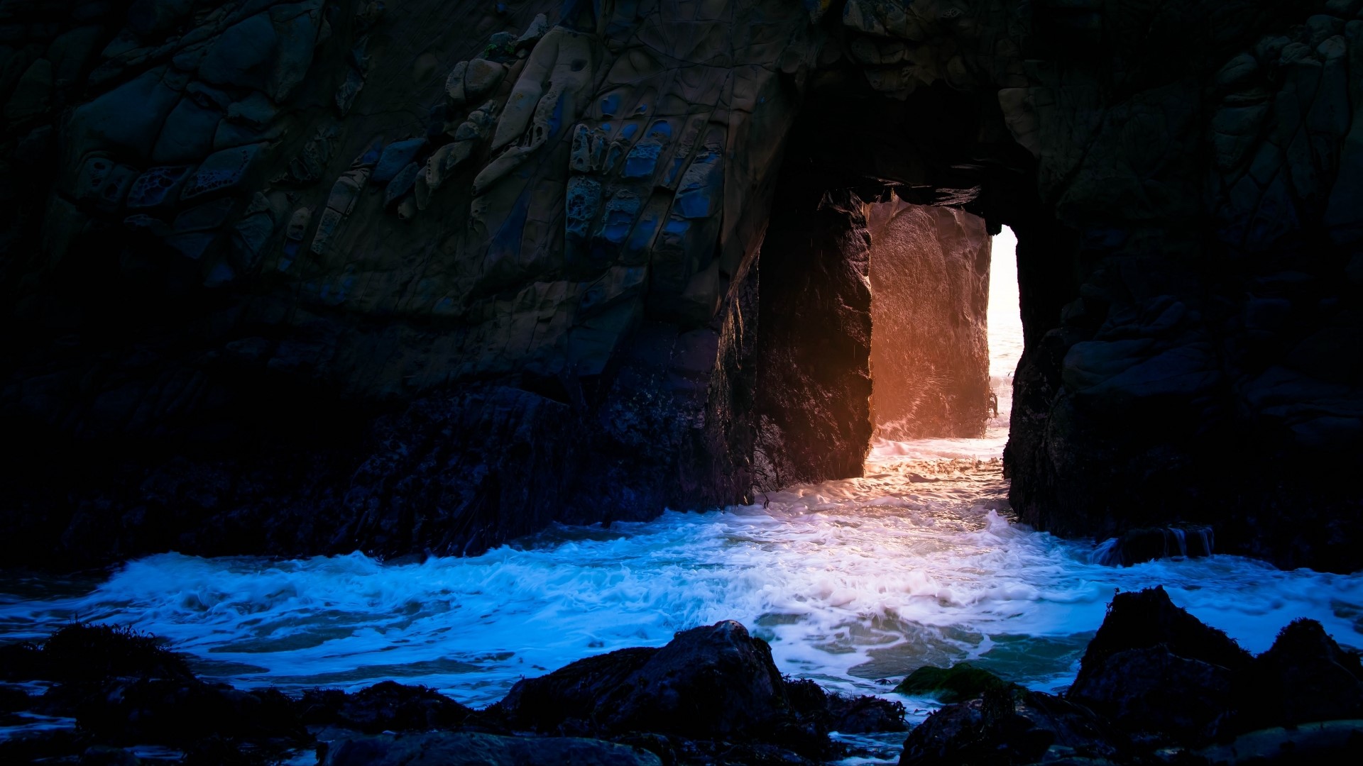 Ocean waves crashing into a dark cave entrance HD Wallpaper