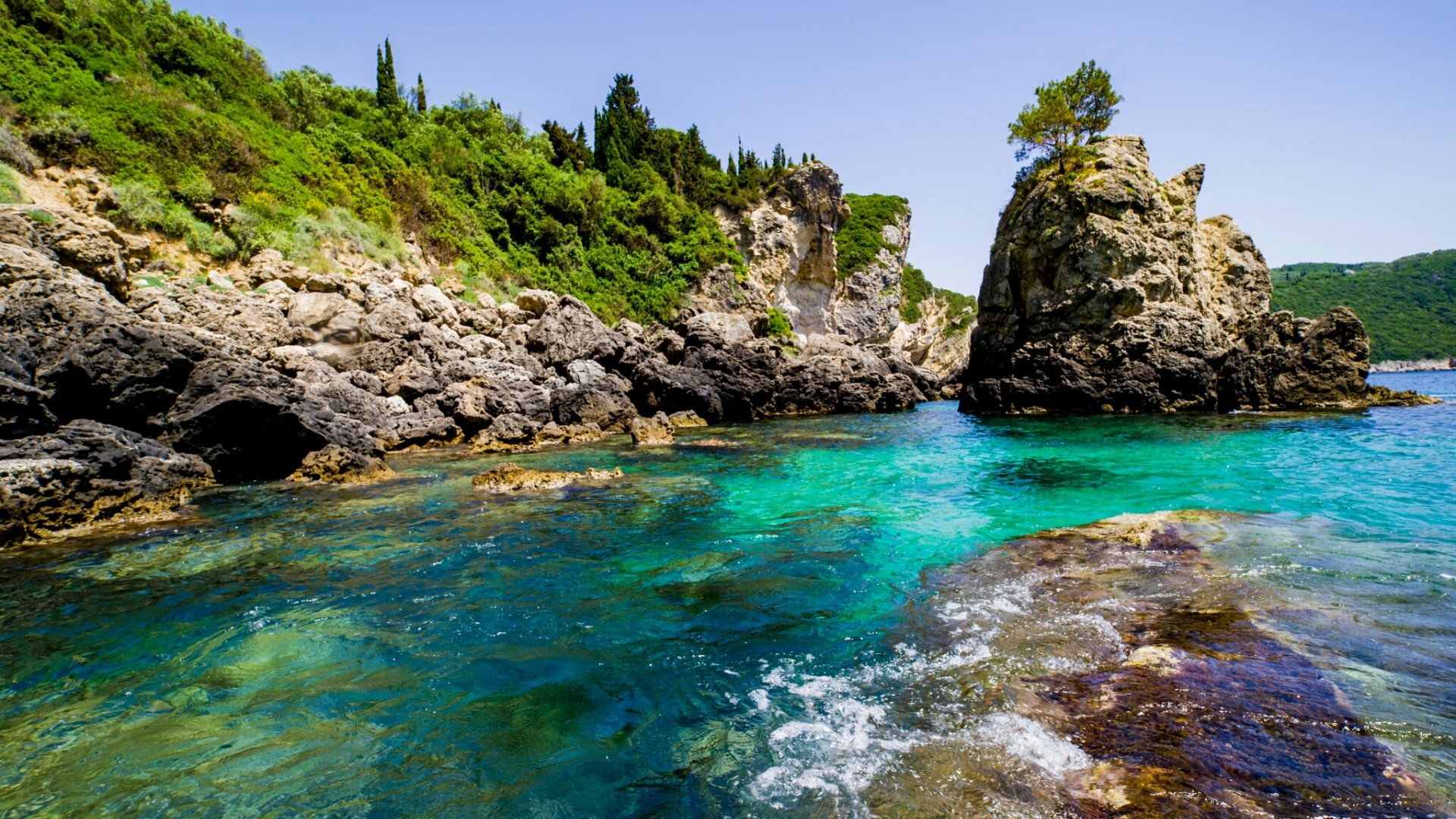 Rocky coastline with turquoise water and lush green hills HD Wallpaper