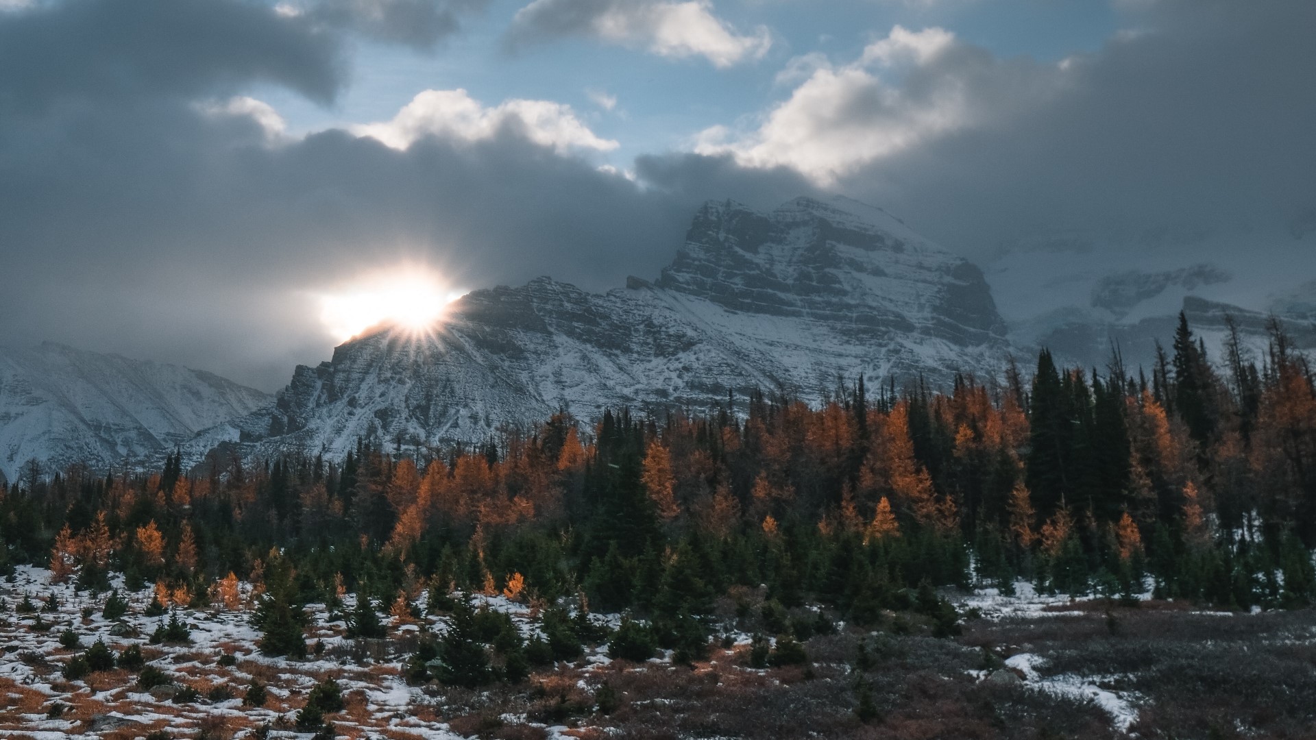 Sunlight breaking through clouds over snowy mountains and autumn forest HD Wallpaper