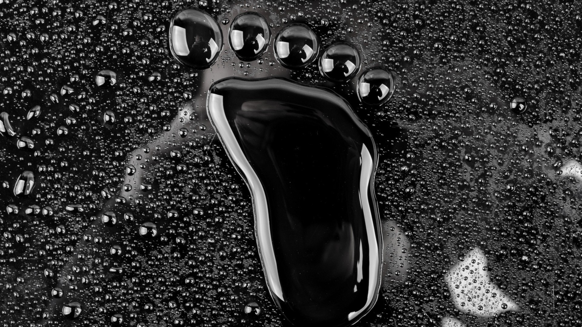 Footprint made of black liquid on a surface with water droplets HD Wallpaper