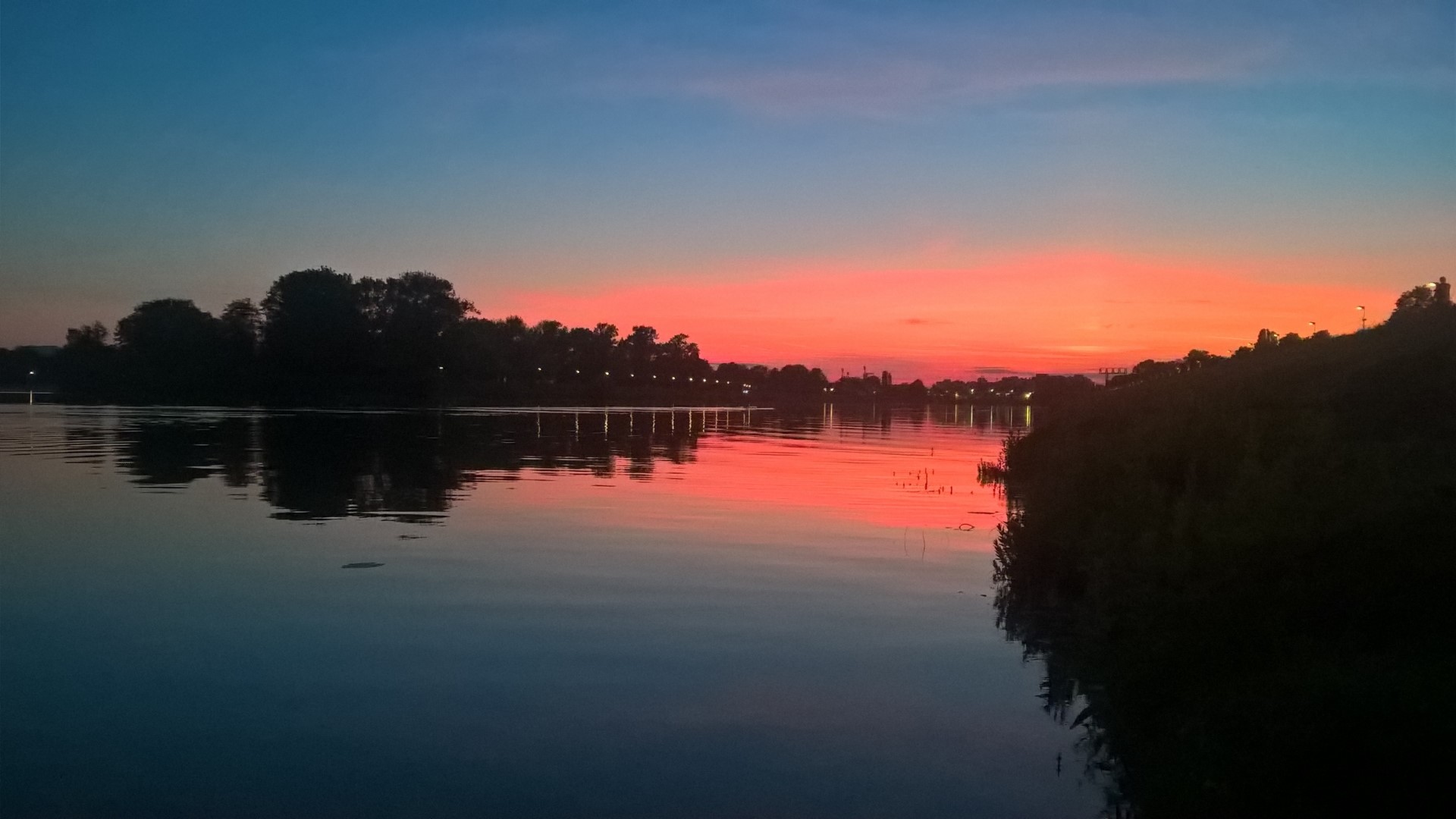 Sunset over a calm lake with trees and a bridge HD Wallpaper