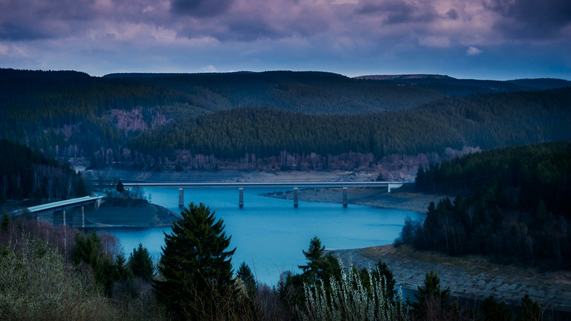 Bridge over a blue lake with forested hills HD Wallpaper