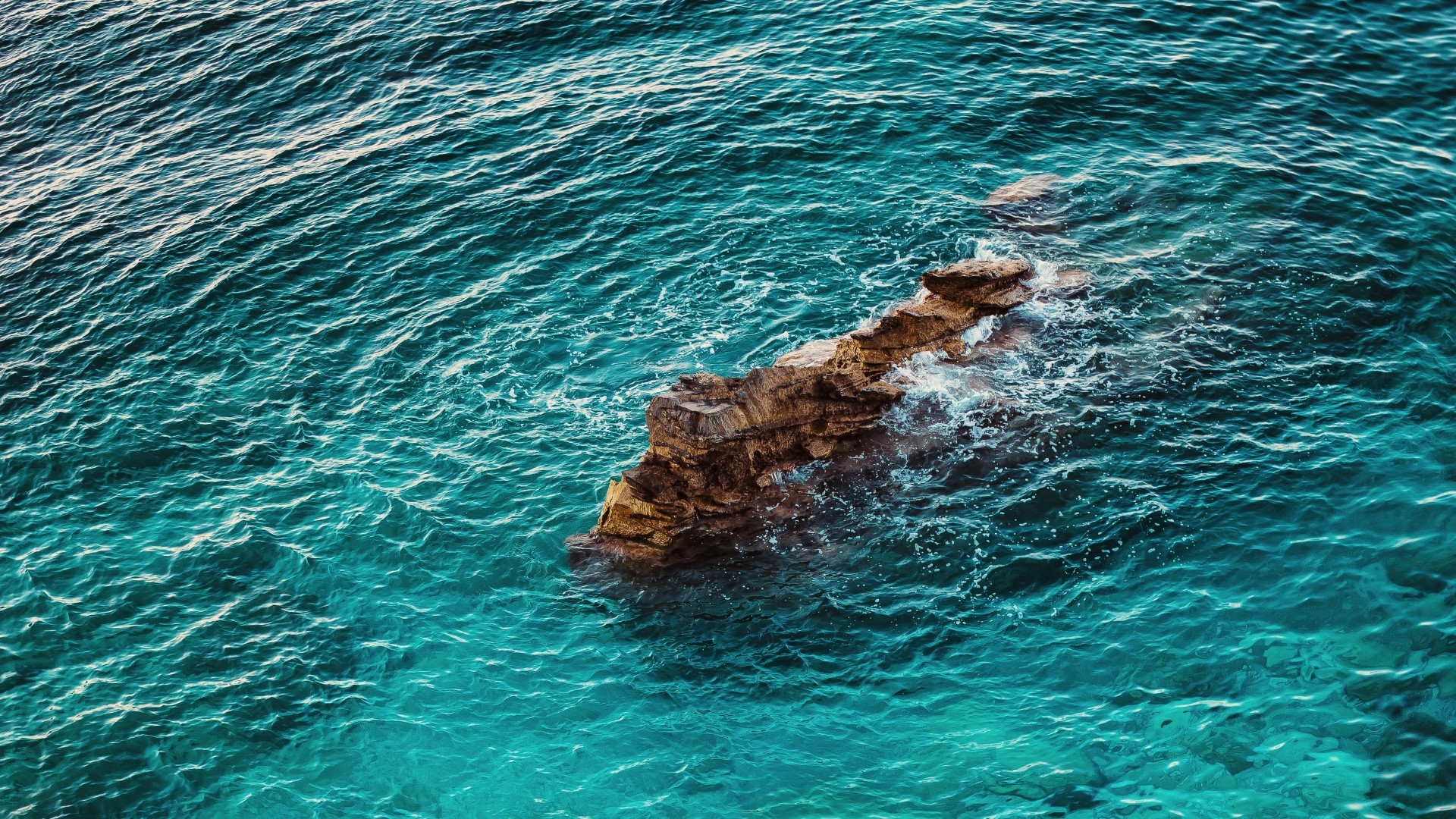 Rocky outcrop in turquoise ocean waves HD Wallpaper