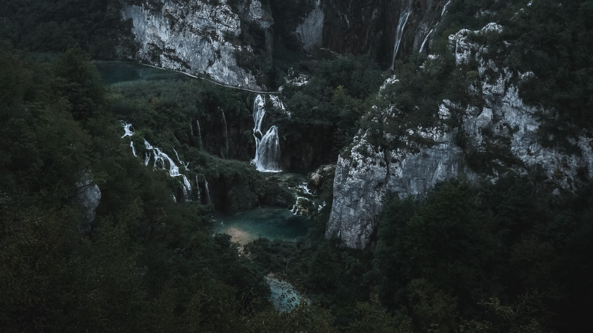 Waterfalls cascading down rocky cliffs surrounded by dense forest HD Wallpaper