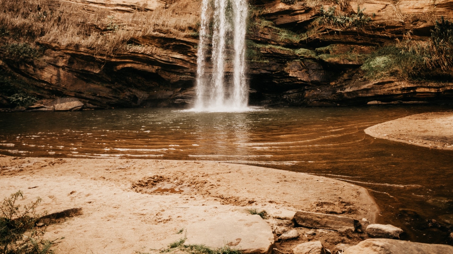 Waterfall cascading into a pool with sandy shore HD Wallpaper