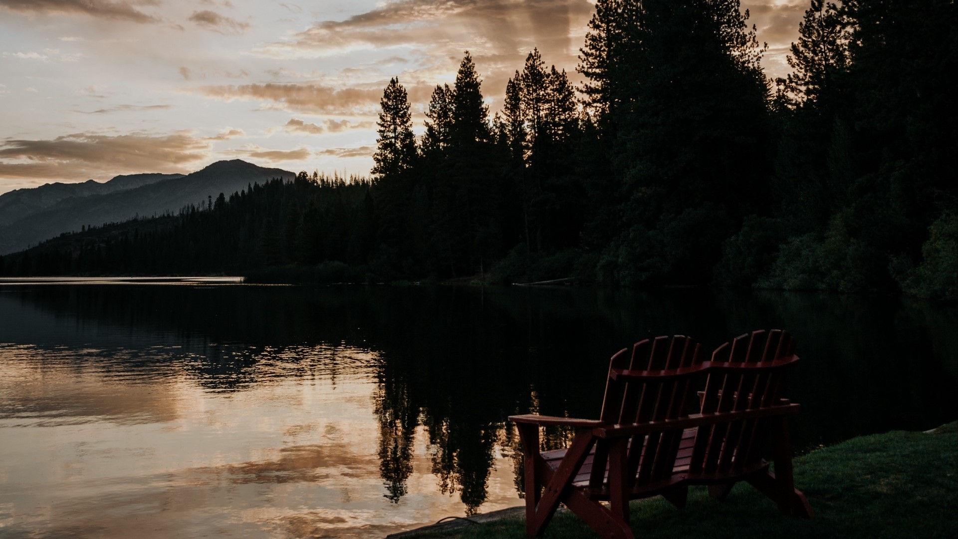 Two Adirondack chairs by a lake at sunset HD Wallpaper