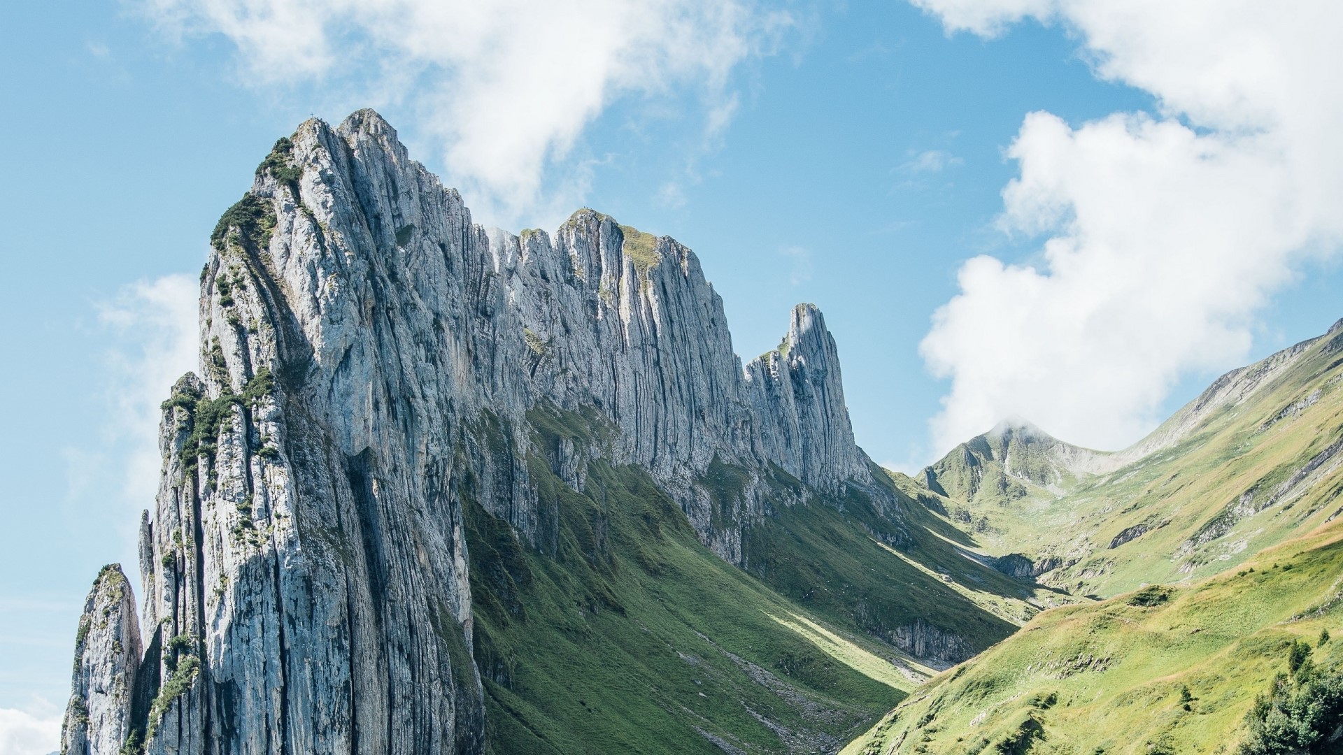 Jagged mountain peaks with green slopes under a cloudy sky HD Wallpaper